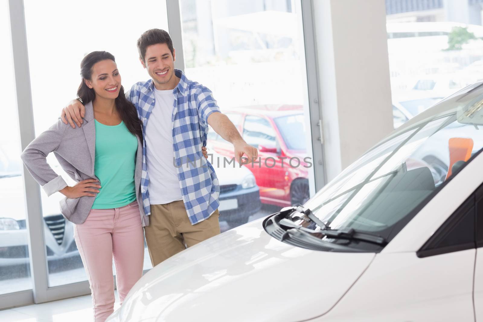 Smiling couple pointing a car at new car showroom