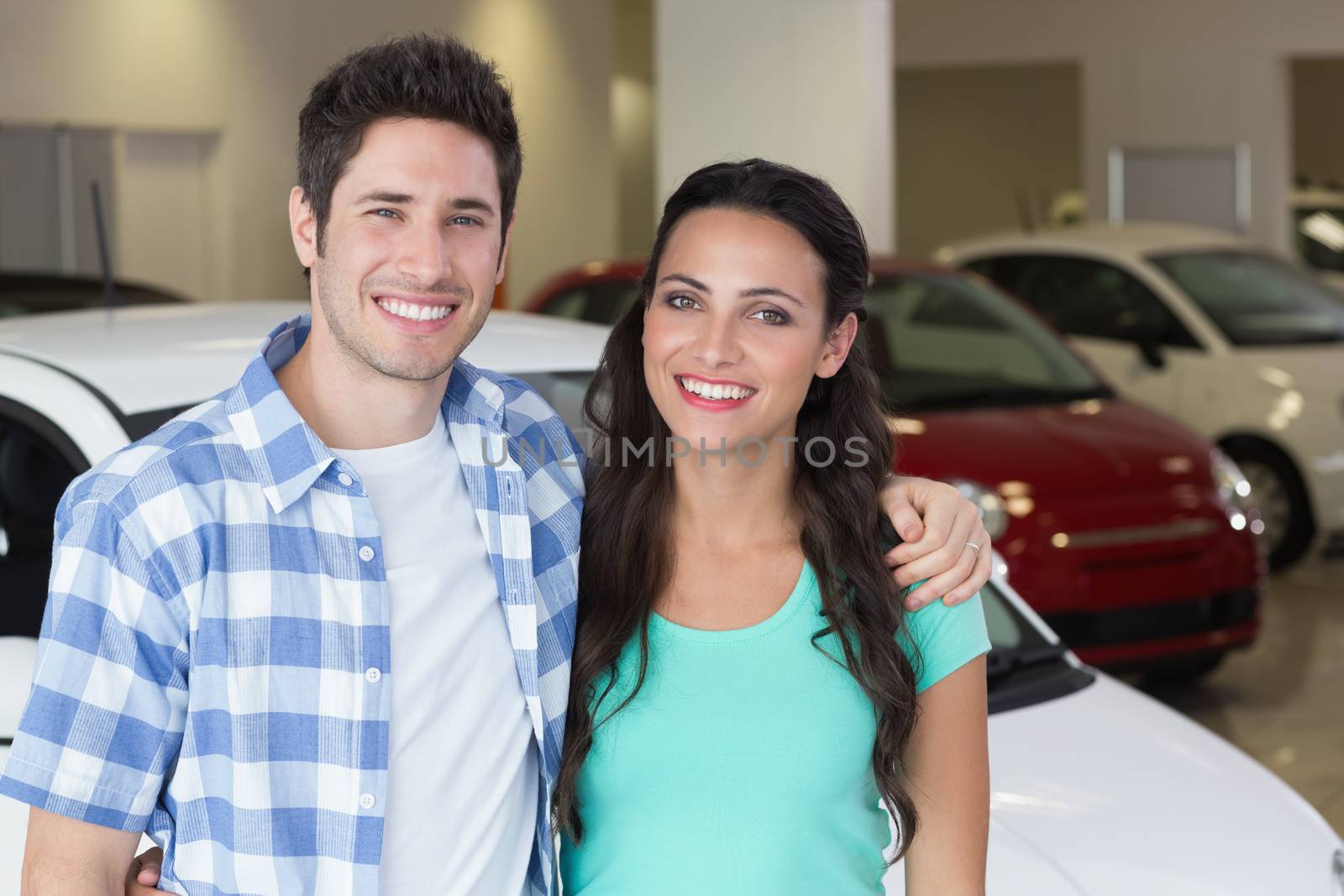 Smiling couple standing in front of a car at new car showroom