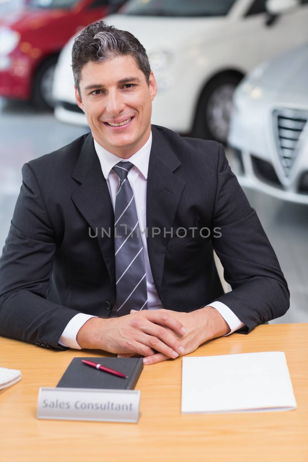 Cheerful businessman working at his desk at new car showroom