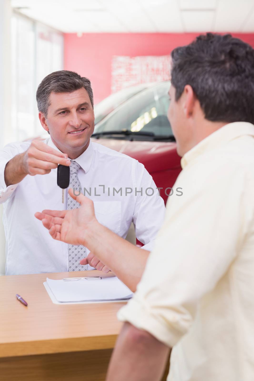 Smiling salesman giving a customer car keys at new car showroom