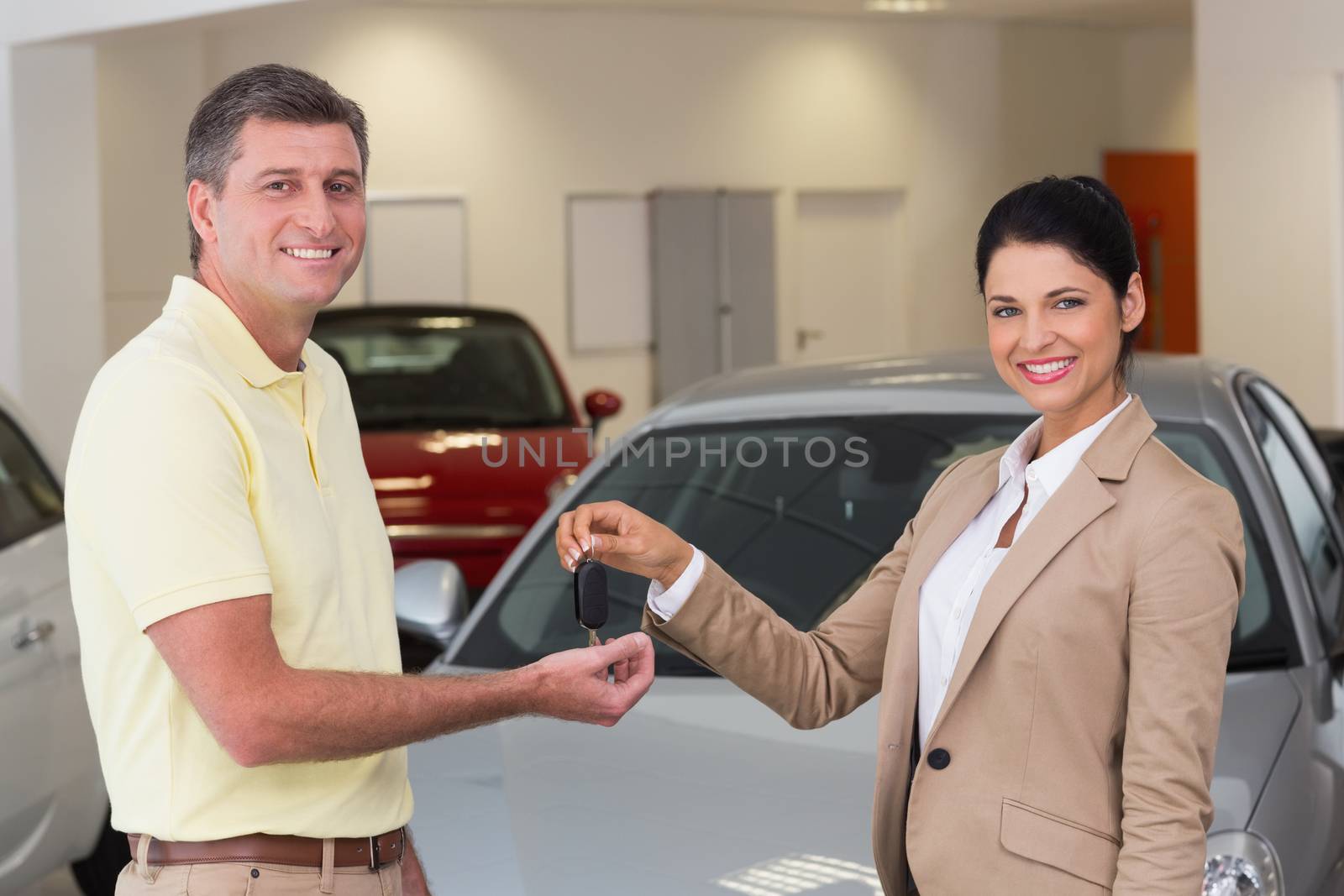 Smiling businesswoman giving car key to happy customer at new car showroom