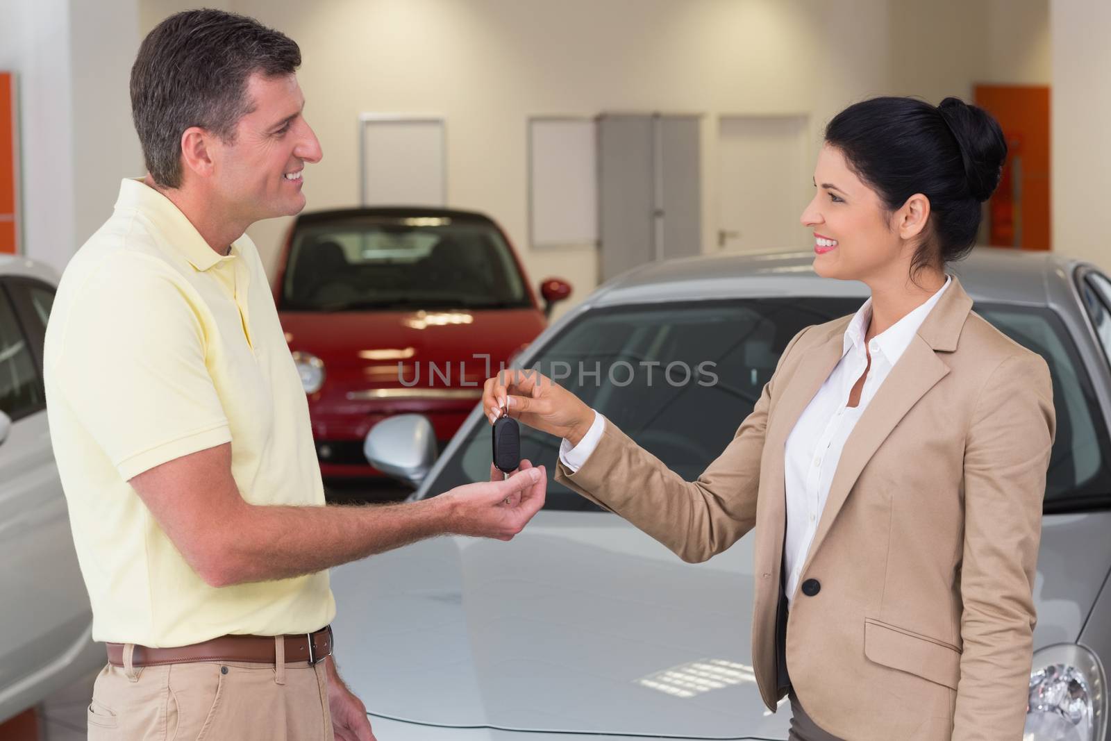 Smiling businesswoman giving car key to happy customer at new car showroom