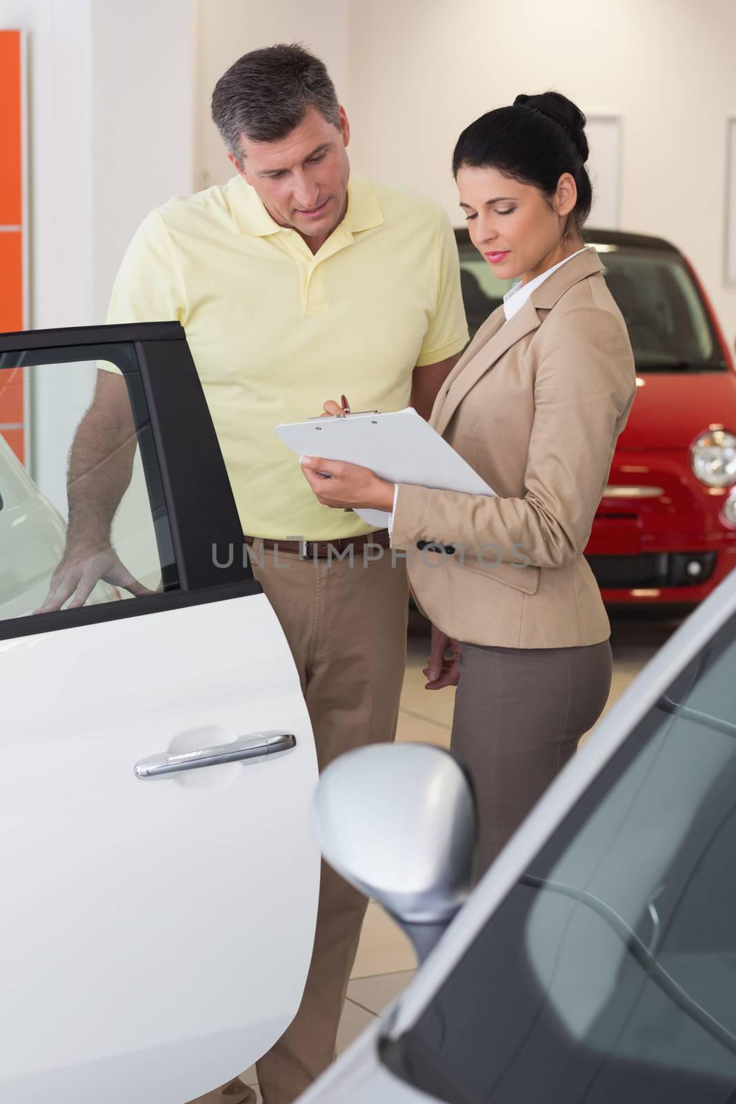 Salesperson showing clipboard to sign to customer at new car showroom