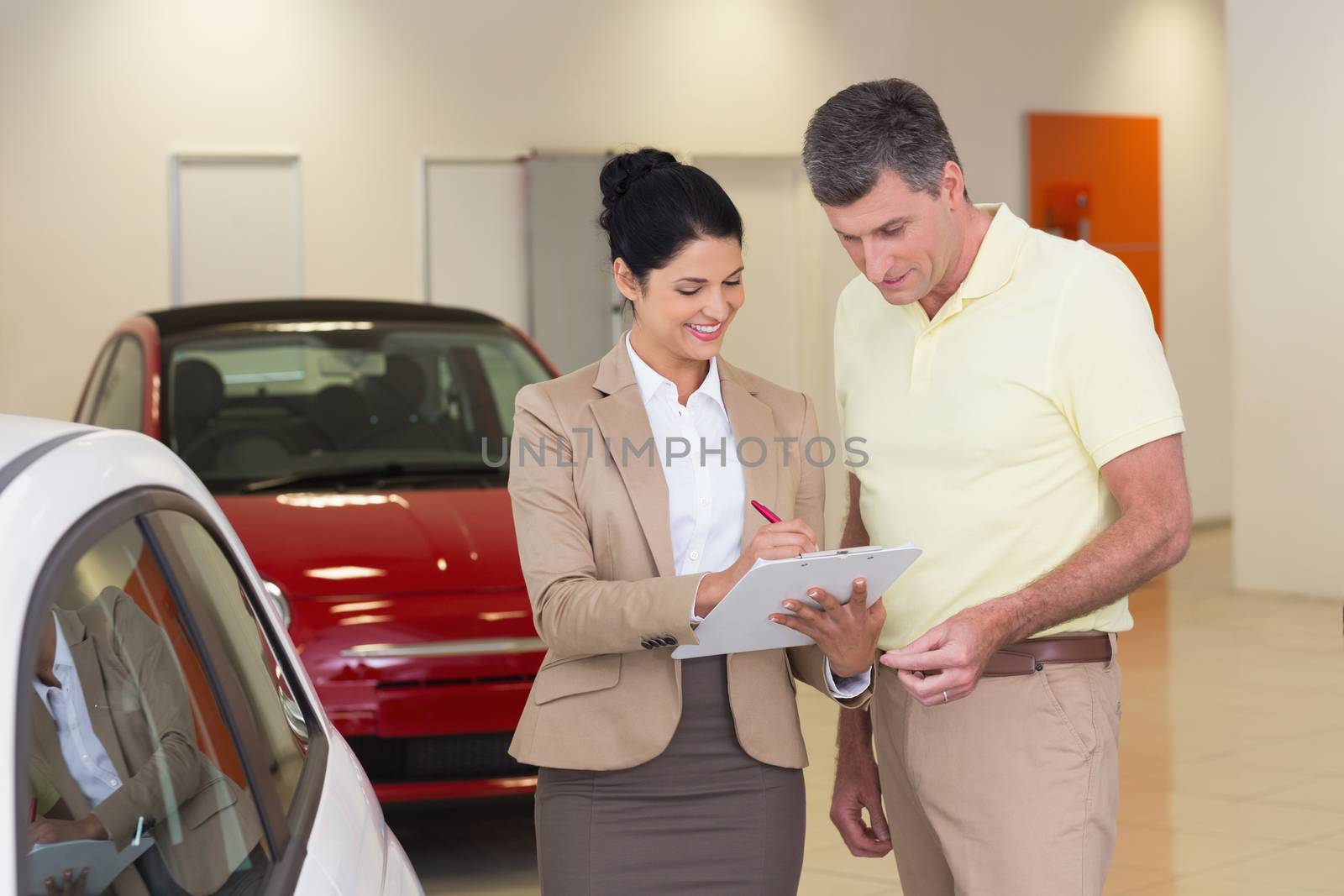Salesperson showing clipboard to sign to customer at new car showroom