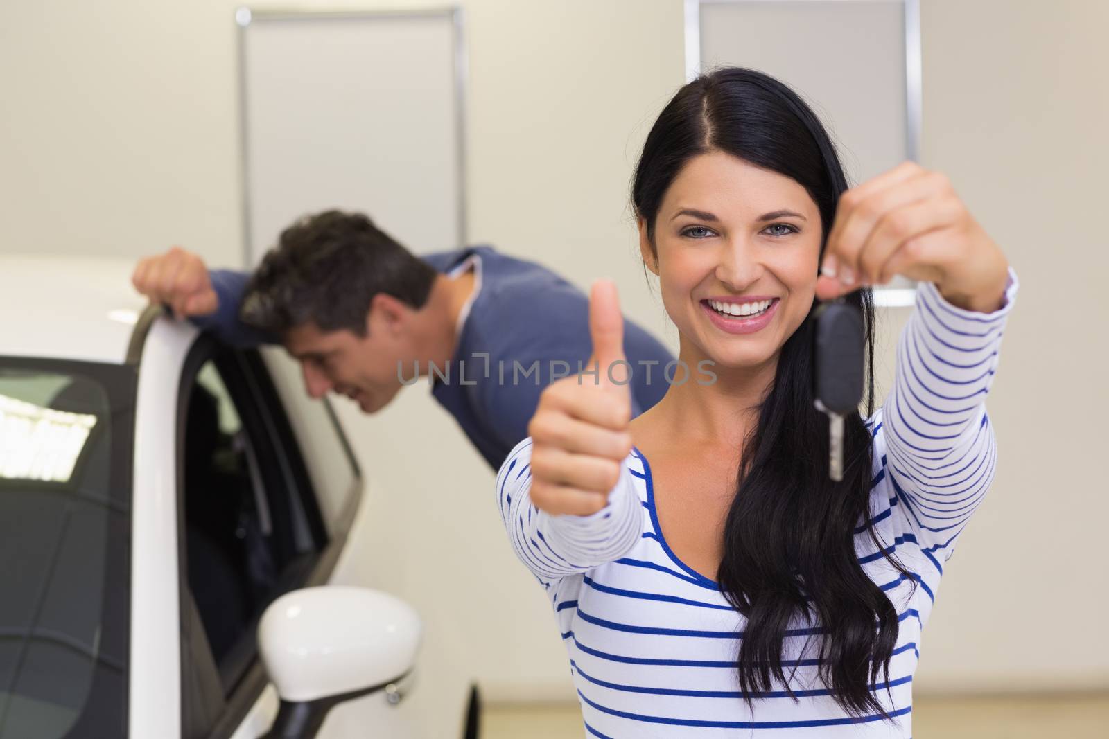 Customer holding her new car key while giving thumbs up at new car showroom