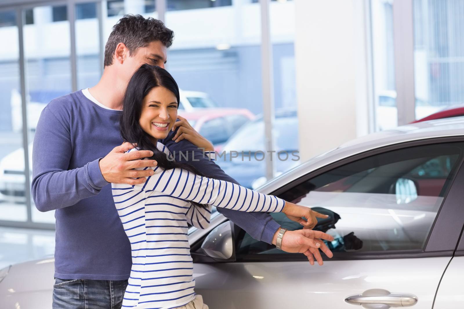 Smiling woman presenting her new car at new car showroom