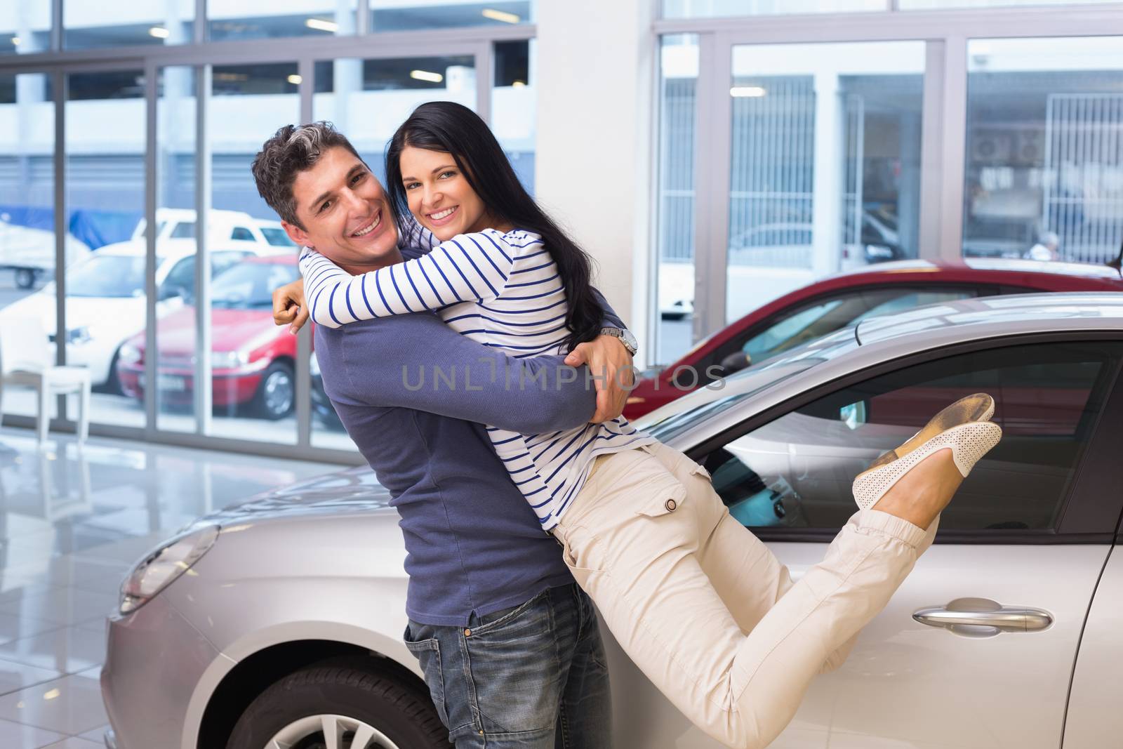 Smiling couple hugging and smiling at camera at new car showroom