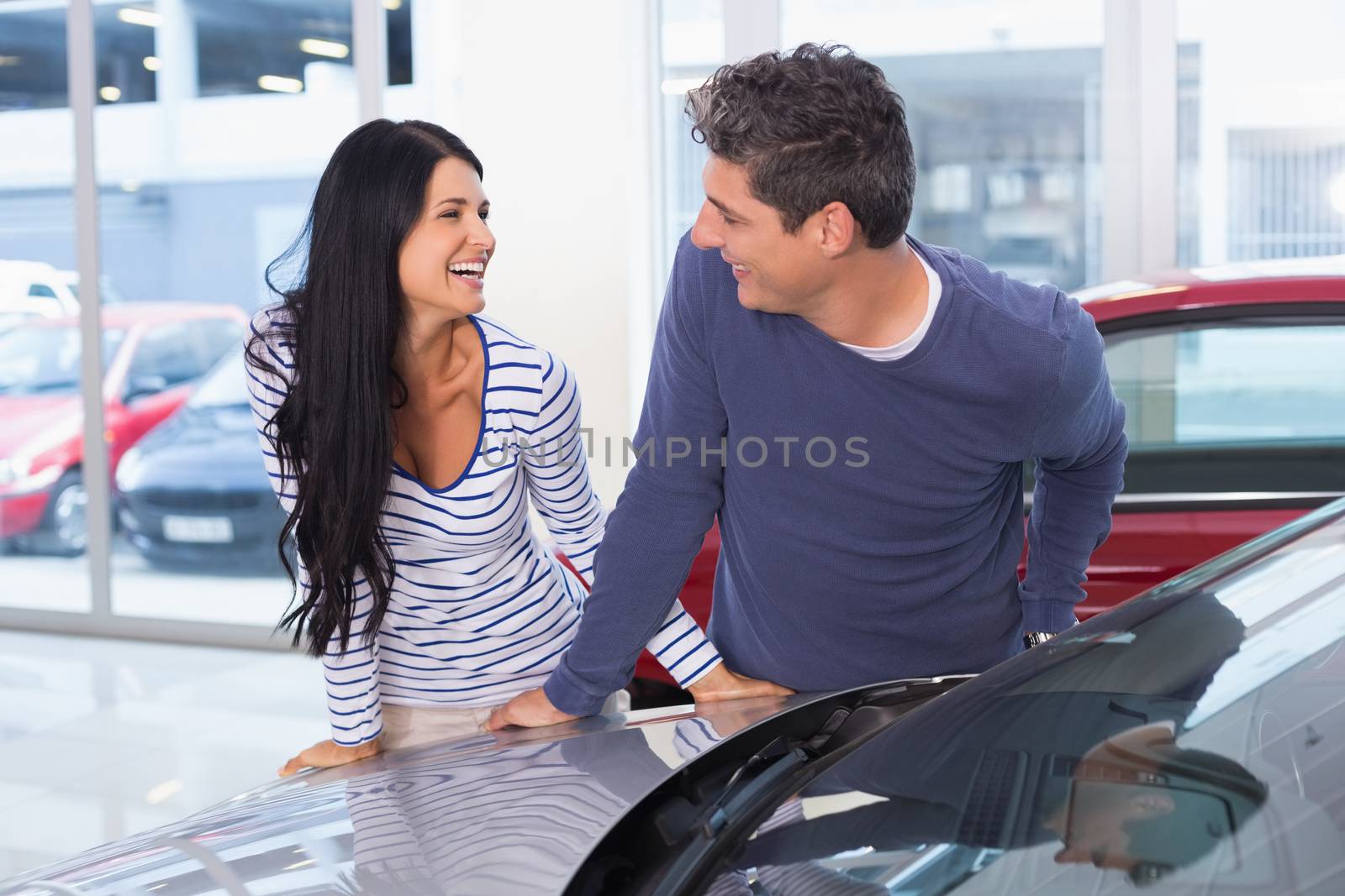 Smiling couple leaning on car at new car showroom