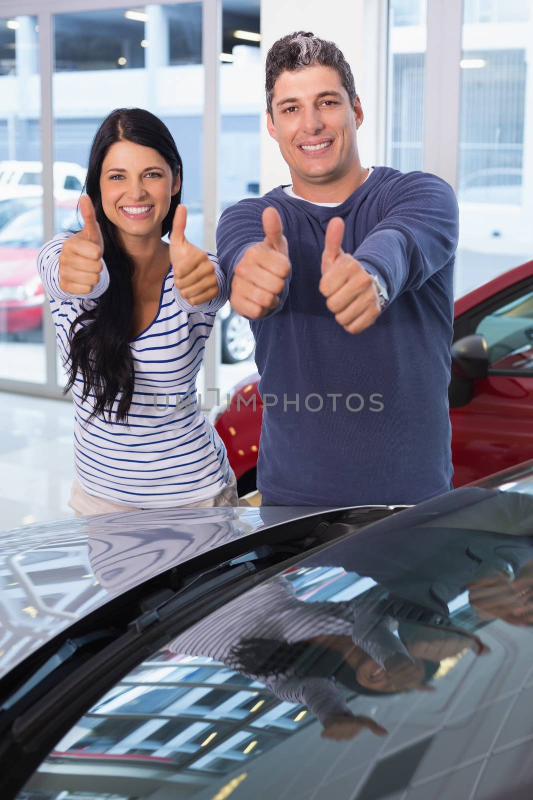 Smiling couple giving thumbs up at new car showroom