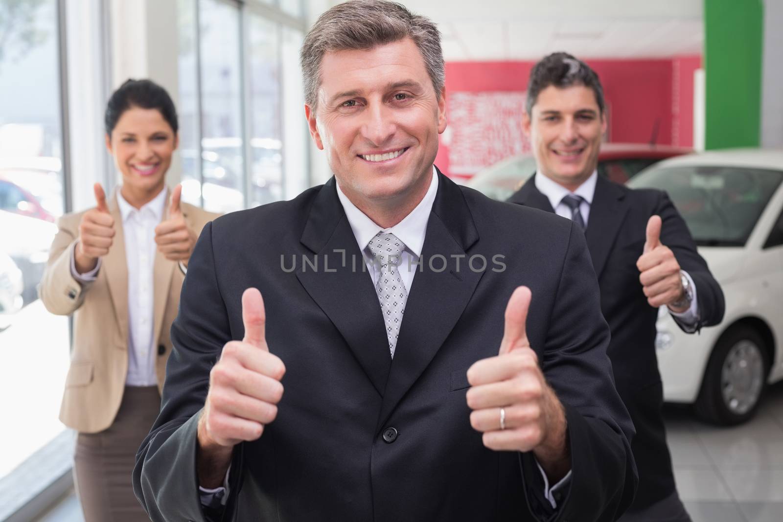 Smiling business team standing while giving thumbs up at new car showroom
