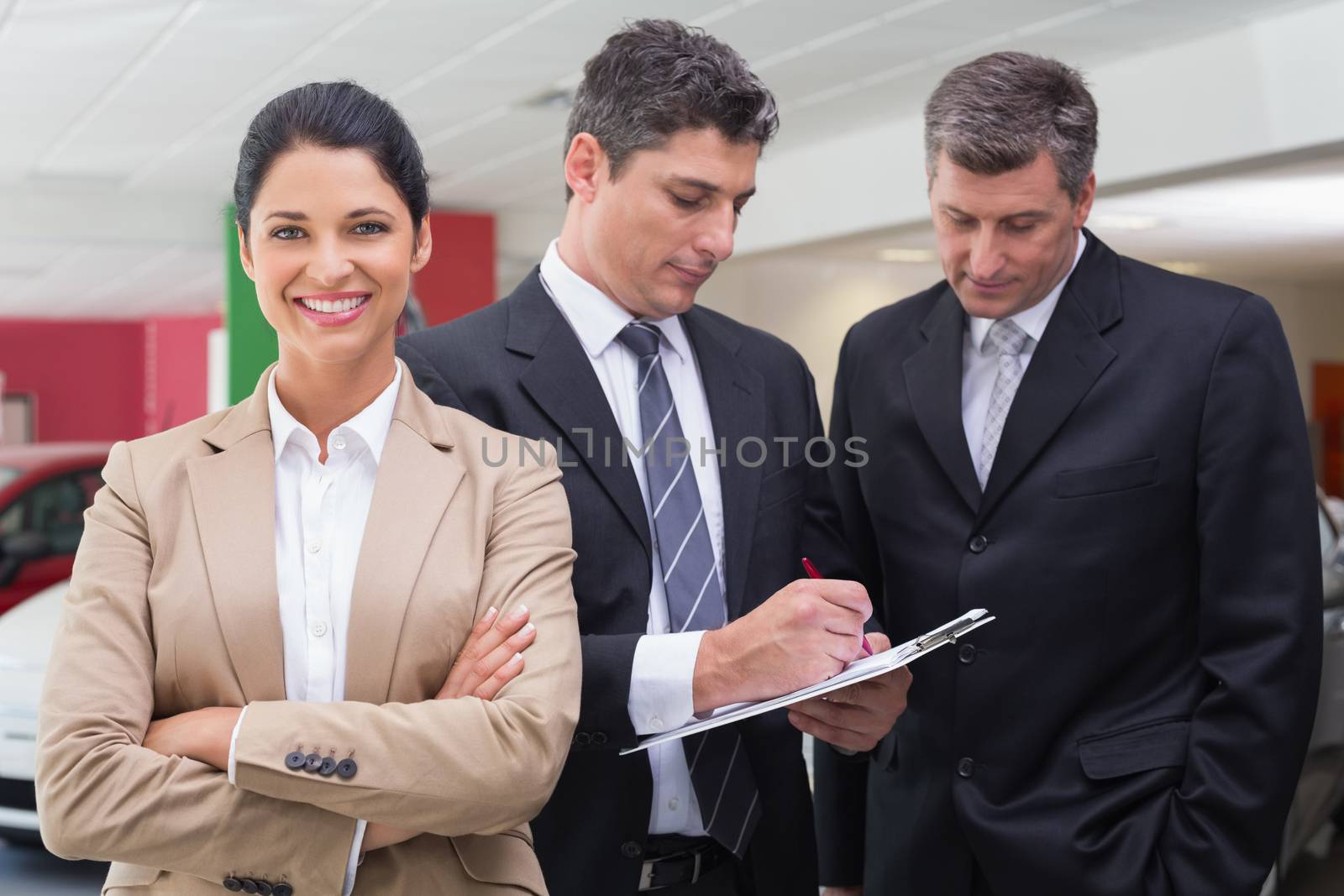 Businessman writing on clipboard talking to colleague at new car showroom