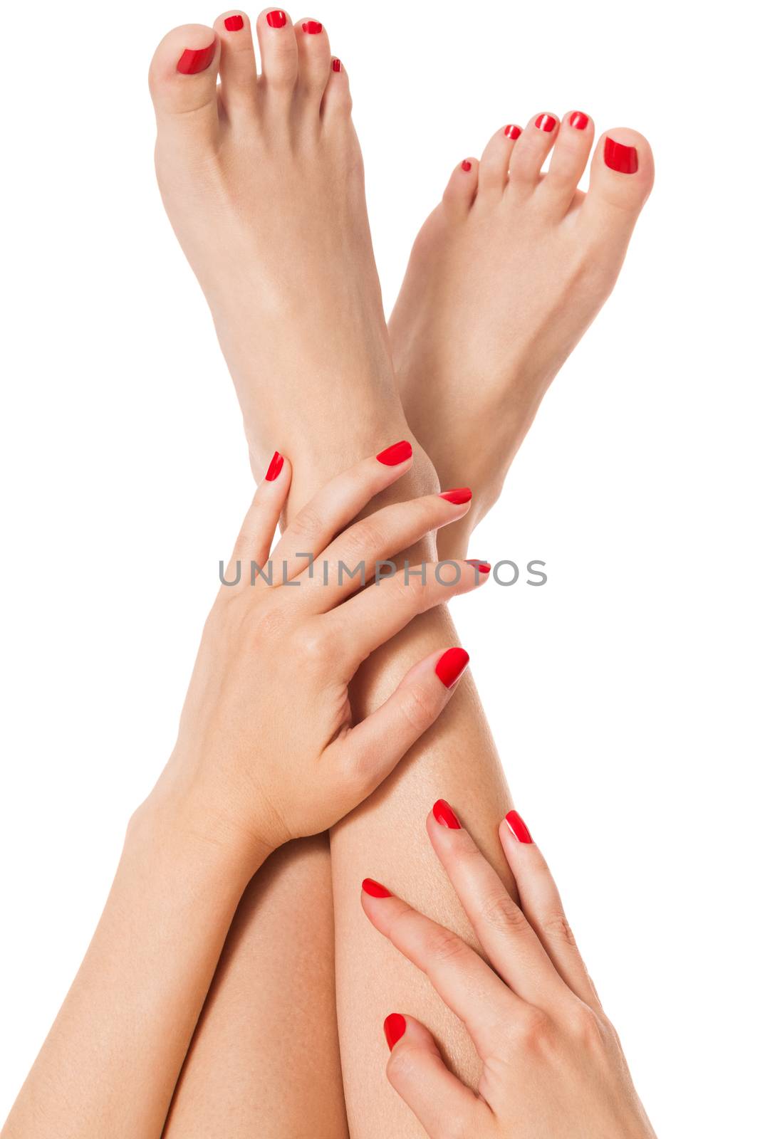 Woman with beautiful neatly manicured red finger and toenails sitting with bare feet clasping her ankles to display her nails, closeup on white in a fashion and beauty concept