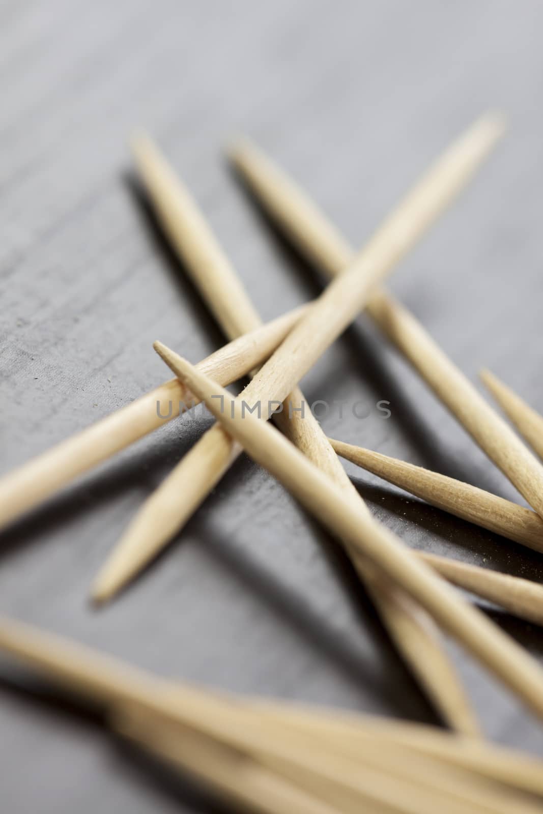 Pile of wooden toothpicks scattered randomly on a grey background for cleaning between the teeth after a meal in a personal hygiene concept