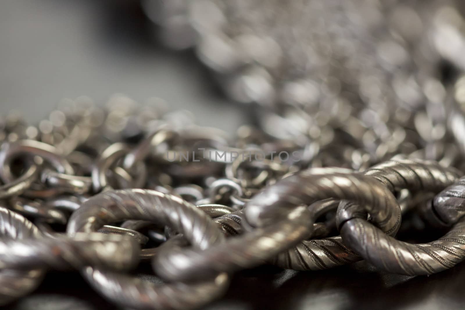 Assorted silver costume jewellery with a jumbled pile of chains with different shaped links, a clear crystal bead and a necklace of round silver beads with focus to the chains