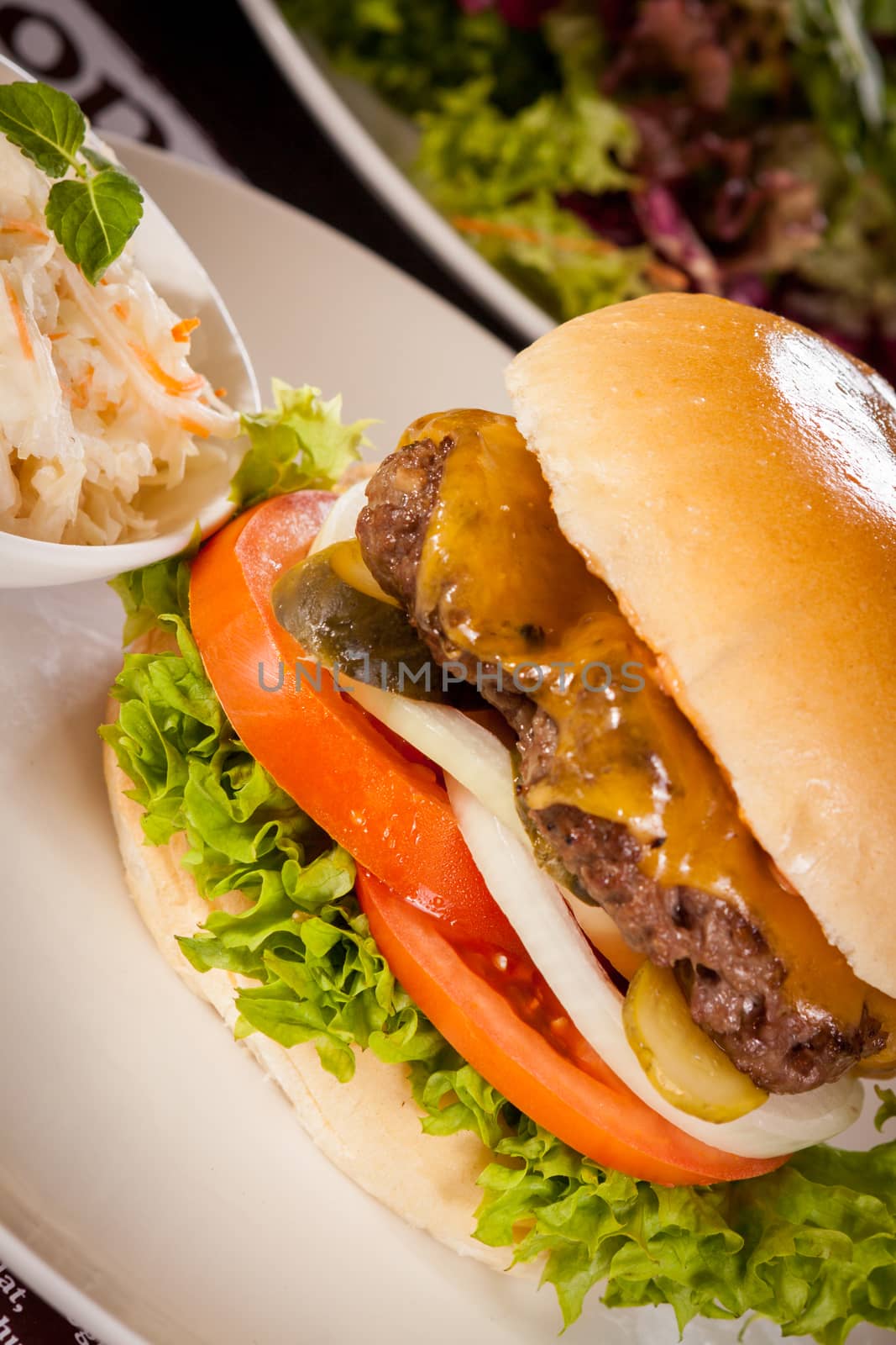 Tasty traditional cheeseburger with a ground beef patty topped with melted cheese and served with onion rings, tomato and curly leaf lettuce on a round white bread roll, close up view