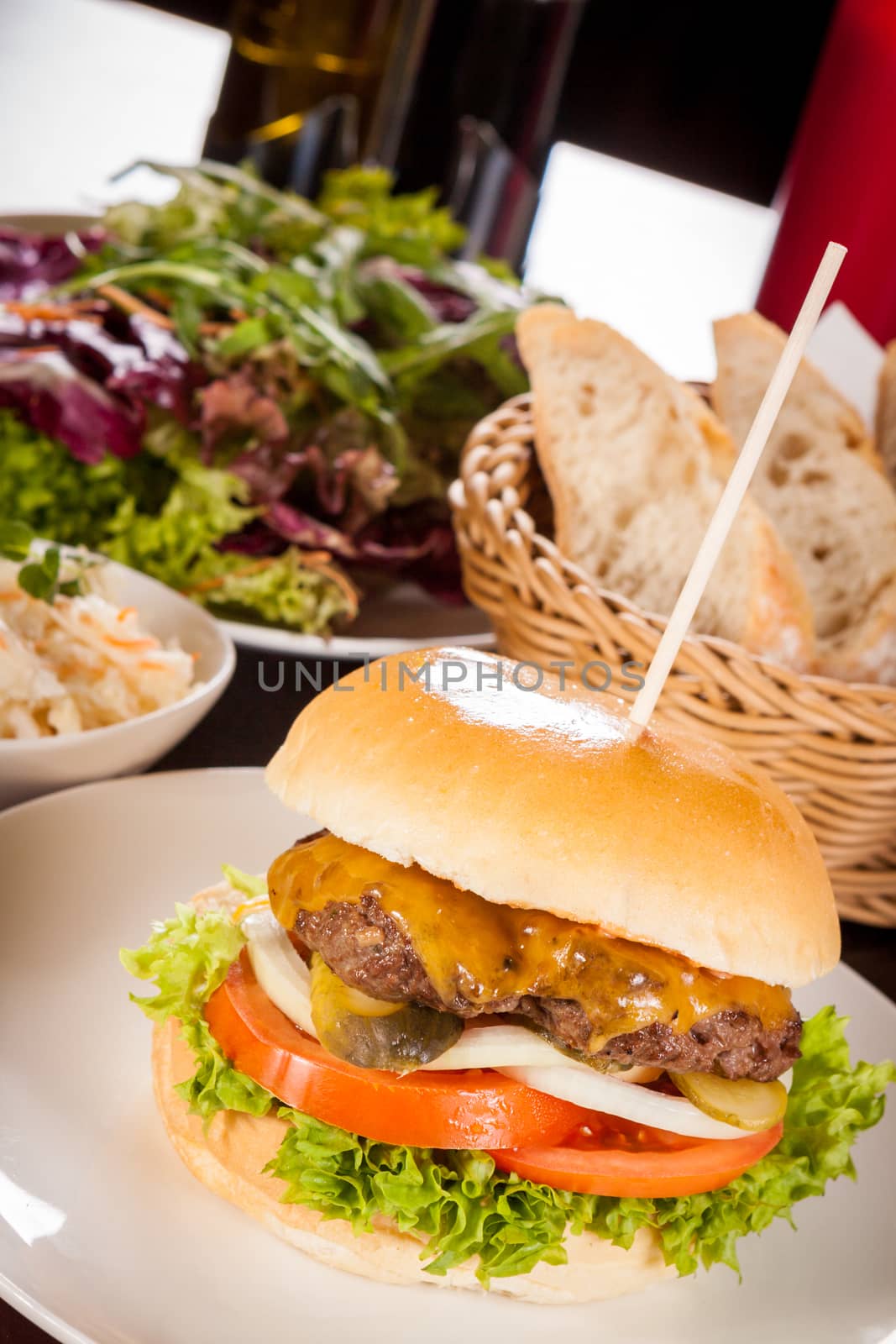 Tasty traditional cheeseburger with a ground beef patty topped with melted cheese and served with onion rings, tomato and curly leaf lettuce on a round white bread roll, close up view