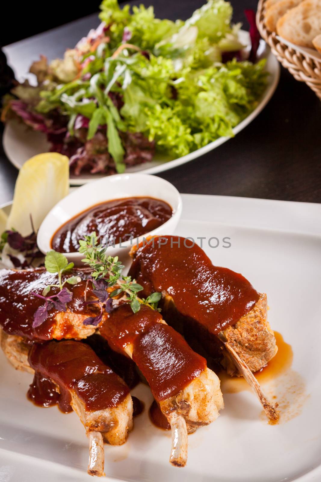 Delicious grilled pork ribs served with a rich brown gravy or BBQ sauce garnished with fresh herbs , close up side view