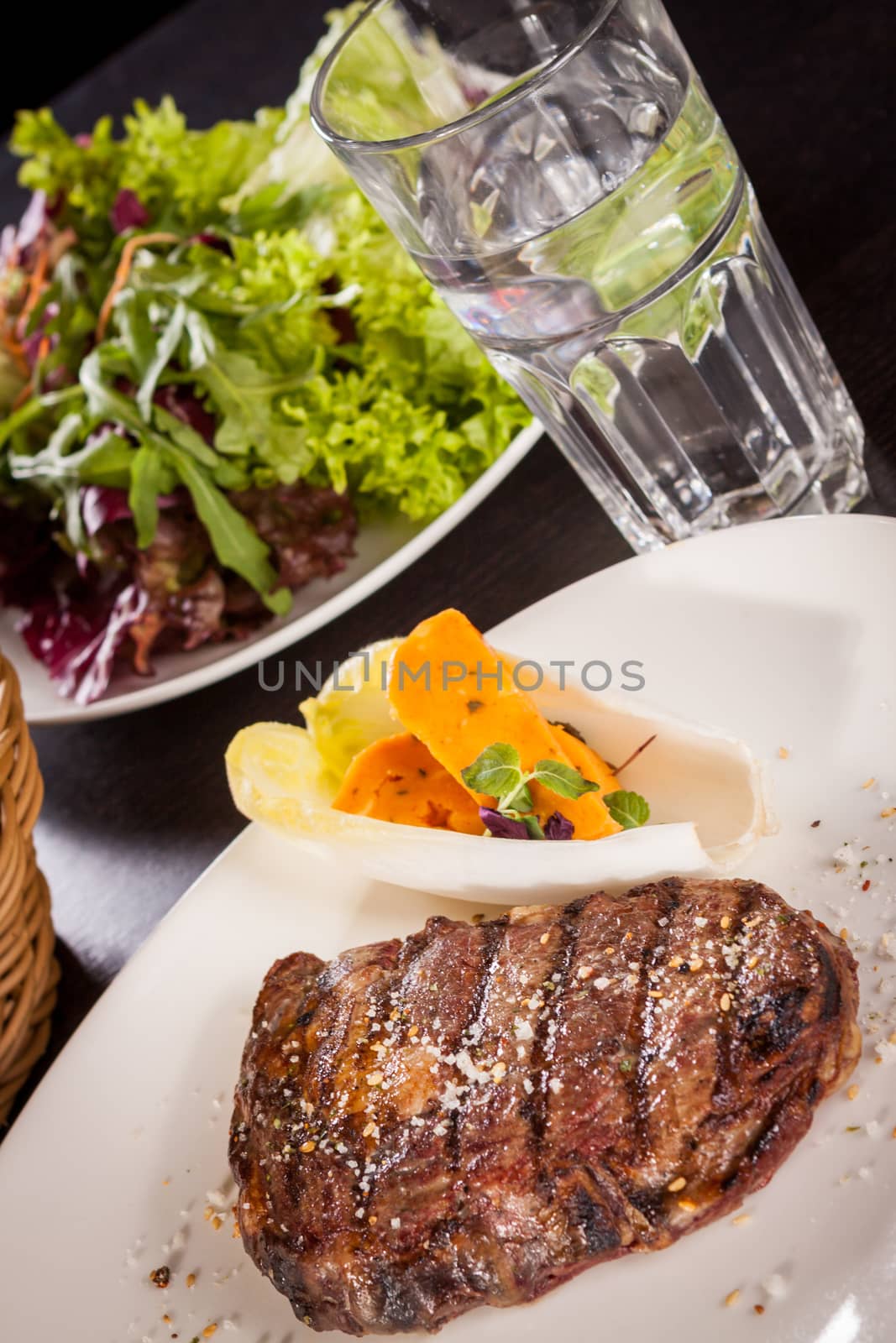 Delicious trimmed lean portion of thick grilled beef steak with seasoning served on a white plate, close up with shallow dof