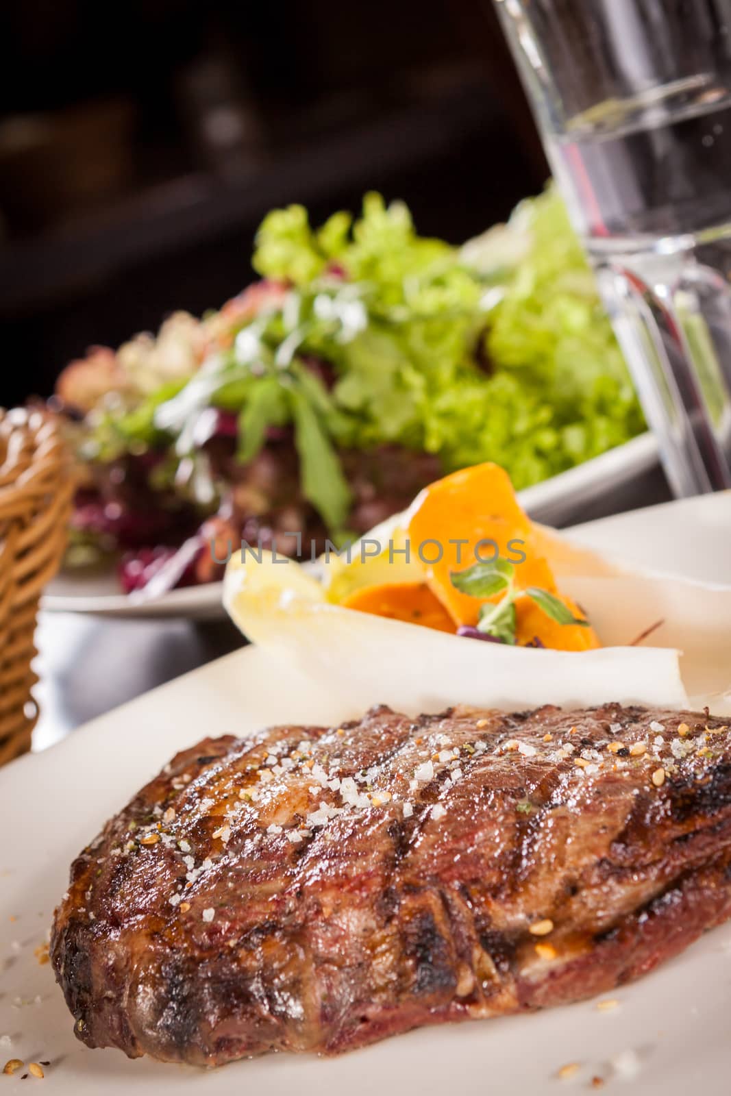 Delicious trimmed lean portion of thick grilled beef steak with seasoning served on a white plate, close up with shallow dof