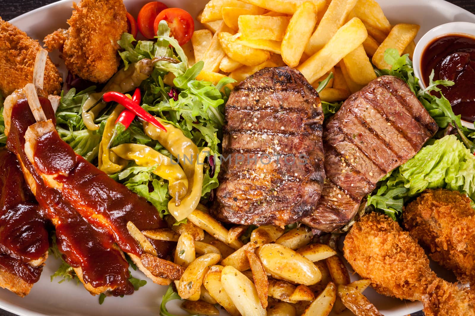 Wholesome platter of mixed meats including grilled steak, crispy crumbed chicken and beef on a bed of fresh leafy green mixed salad served with French fries and chutney or BBQ sauce in a dish