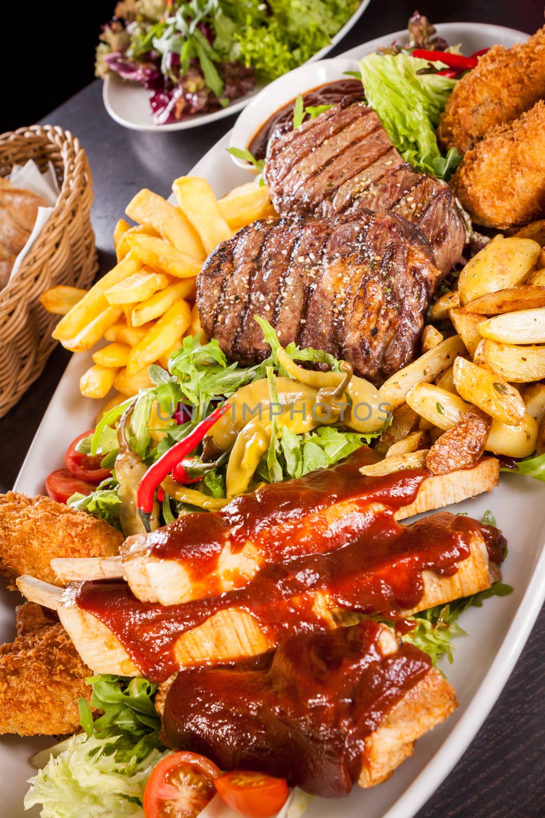 Wholesome platter of mixed meats including grilled steak, crispy crumbed chicken and beef on a bed of fresh leafy green mixed salad served with French fries and chutney or BBQ sauce in a dish