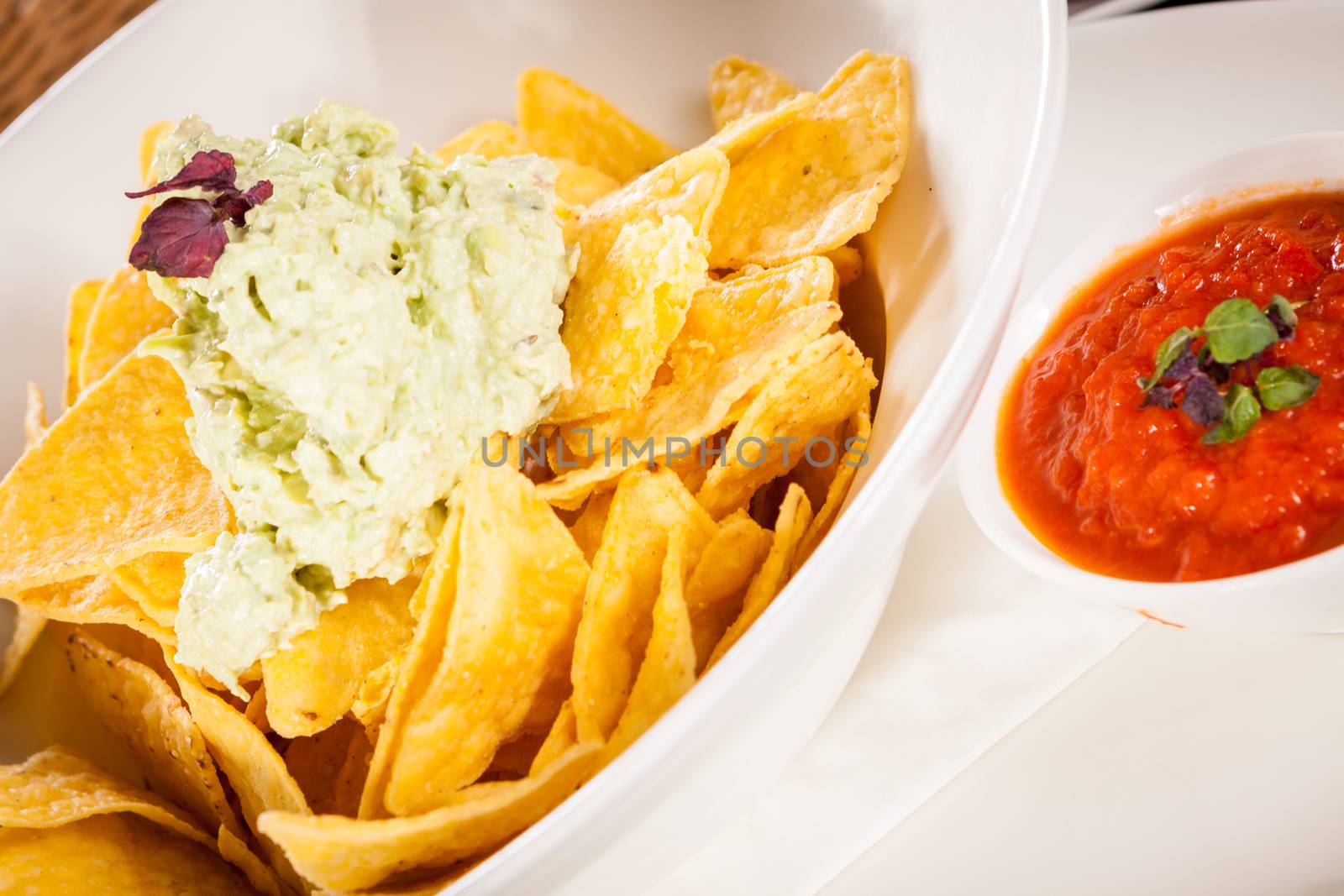 Crisp corn nachos with spicy fresh guacamole sauce and a topping of avocado served as a snack or appetizer in a white bowl