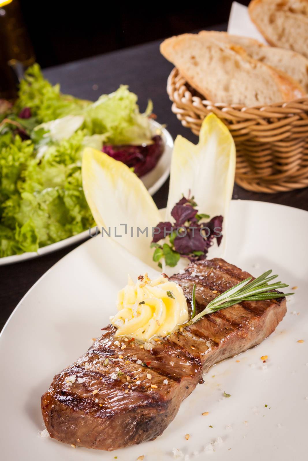 Tasty grilled beef steak topped with a twirled knob of butter and a sprig of fresh rosemary and served on a white plate, close up view