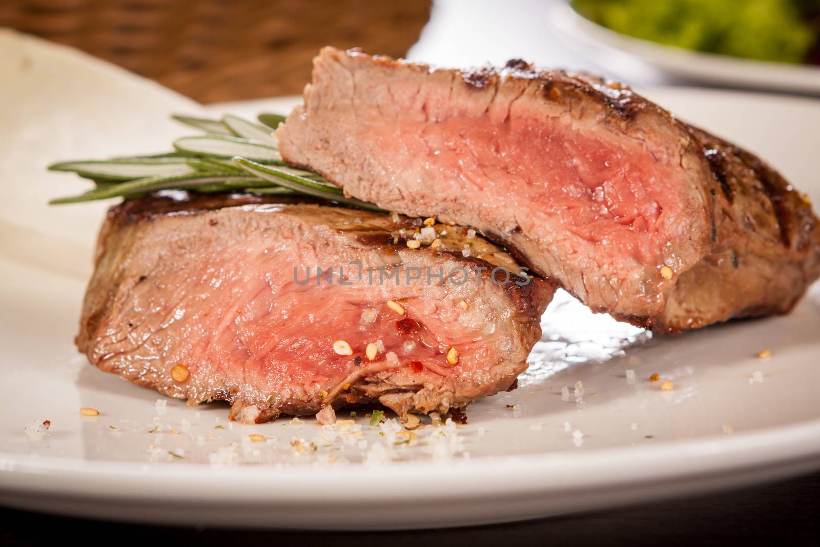 Succulent medium rare beef steak sliced through to display the tender red flesh and seasoned with spices and fresh rosemary, close up view