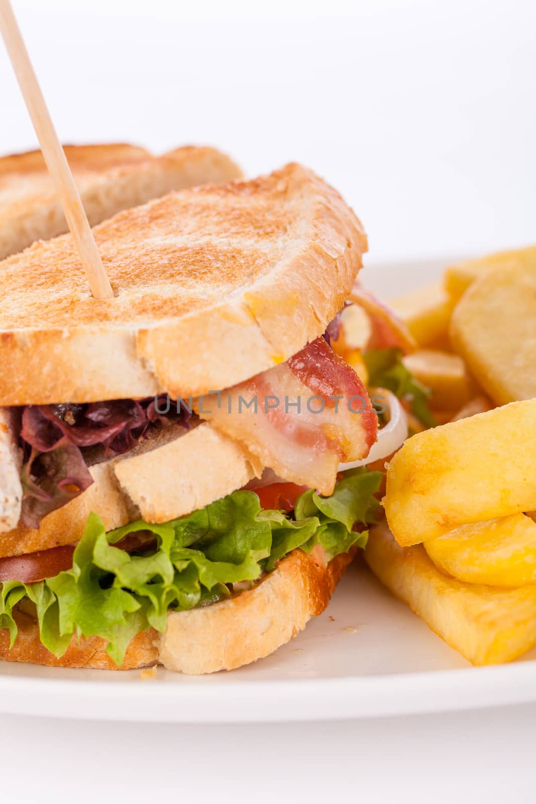 Club sandwich on toasted white bread with a meat filling served with crispy golden potato French fries, closeup partial view isolated on white