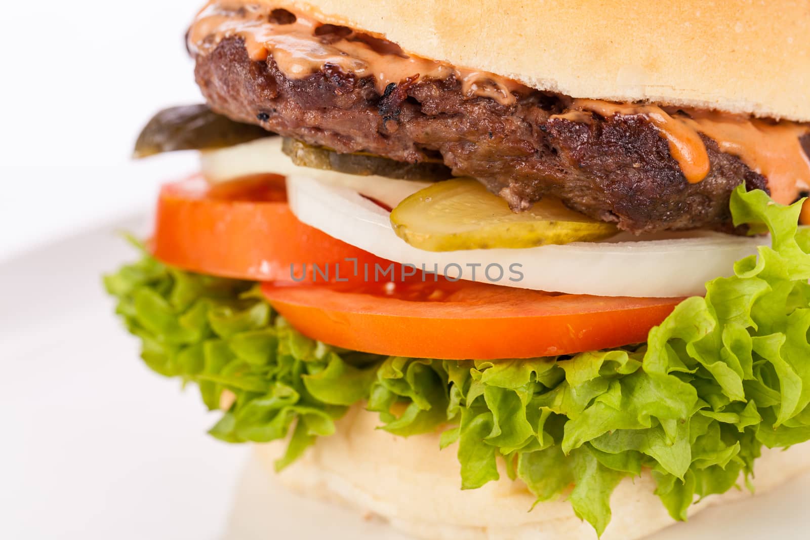 Tasty traditional cheeseburger with a ground beef patty topped with melted cheese and served with onion rings, tomato and curly leaf lettuce on a round white bread roll, close up view