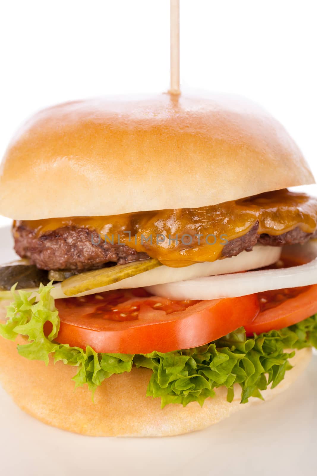 Tasty traditional cheeseburger with a ground beef patty topped with melted cheese and served with onion rings, tomato and curly leaf lettuce on a round white bread roll, close up view