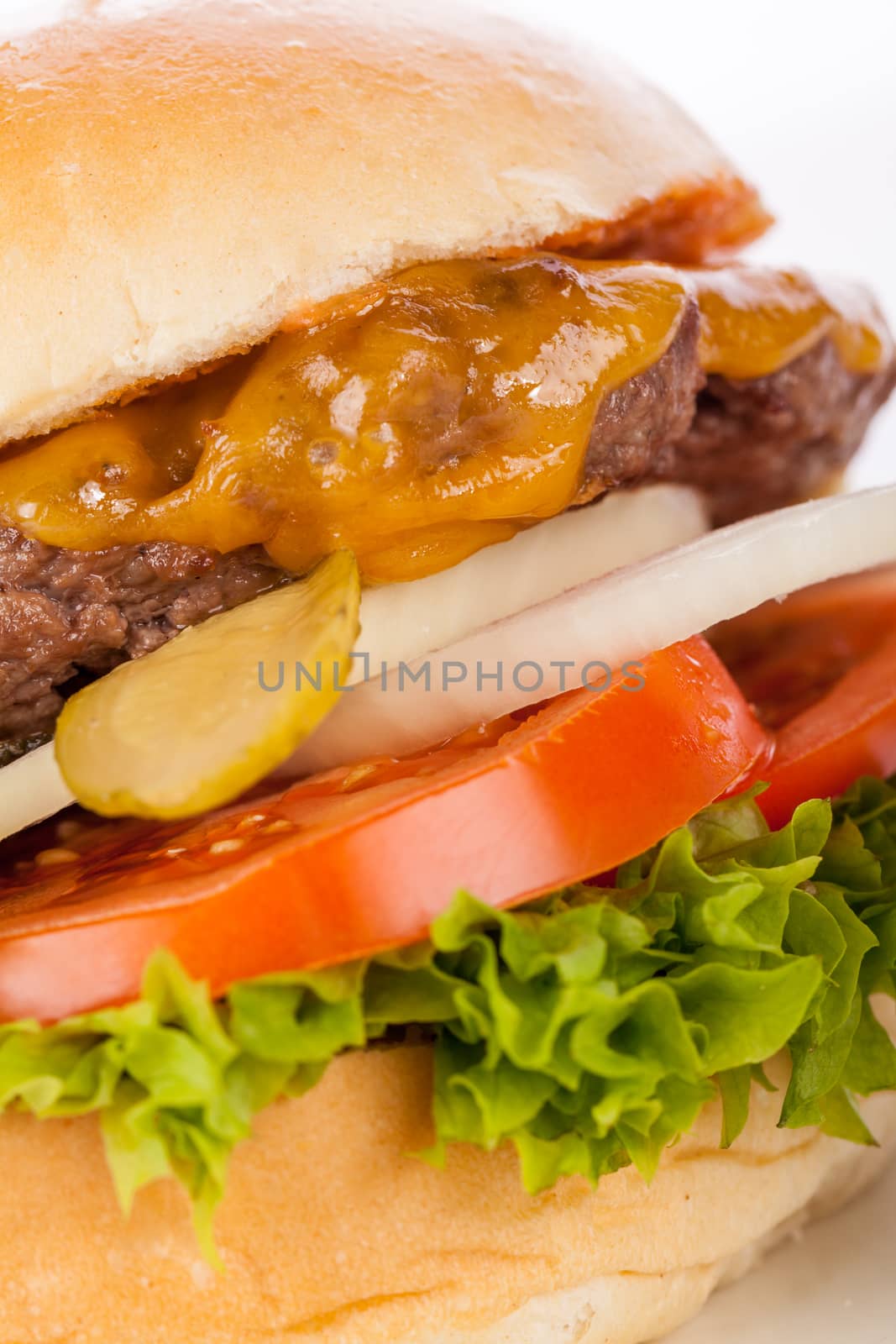 Tasty traditional cheeseburger with a ground beef patty topped with melted cheese and served with onion rings, tomato and curly leaf lettuce on a round white bread roll, close up view