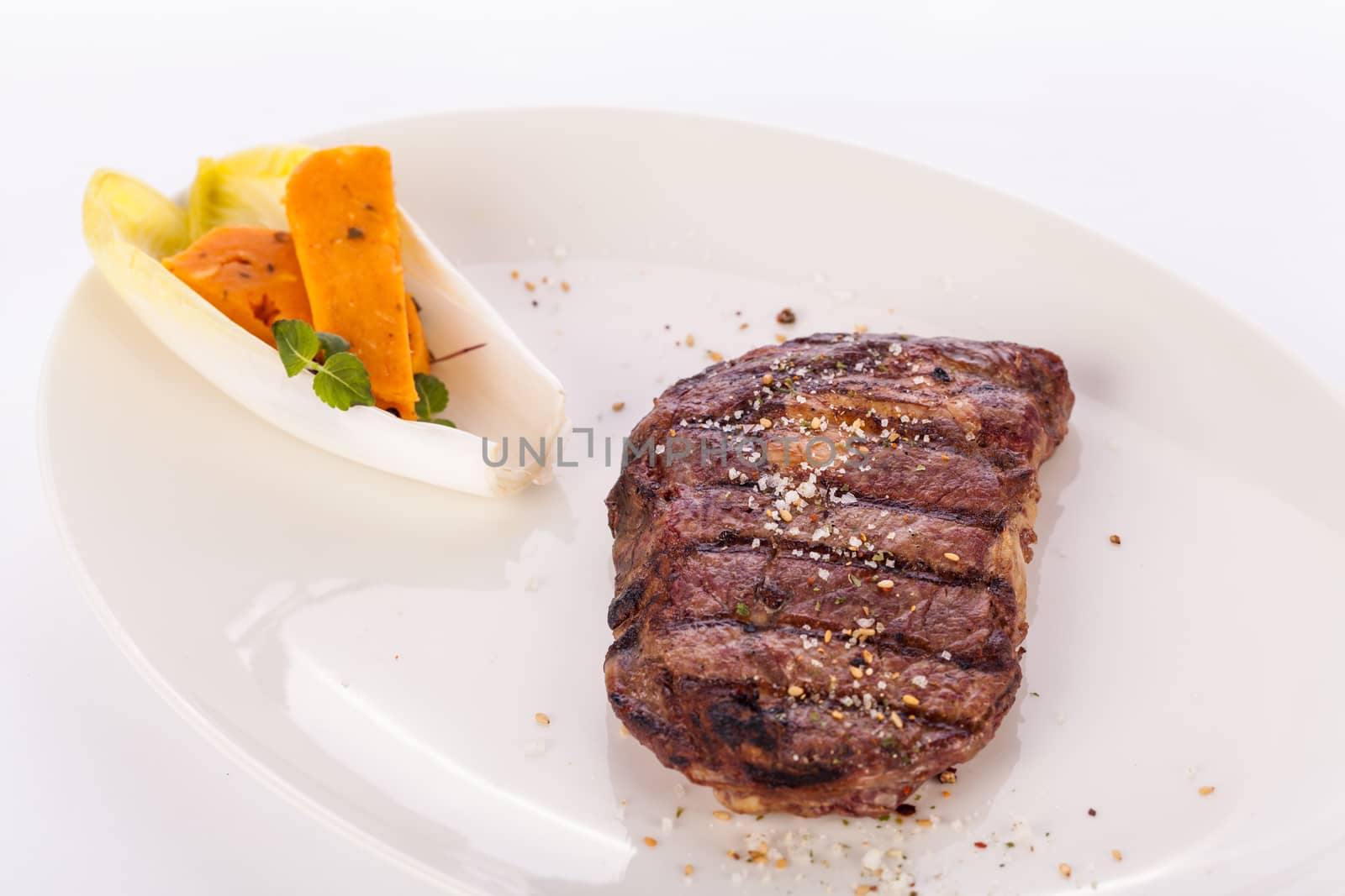 Delicious trimmed lean portion of thick grilled beef steak with seasoning served on a white plate, close up with shallow dof