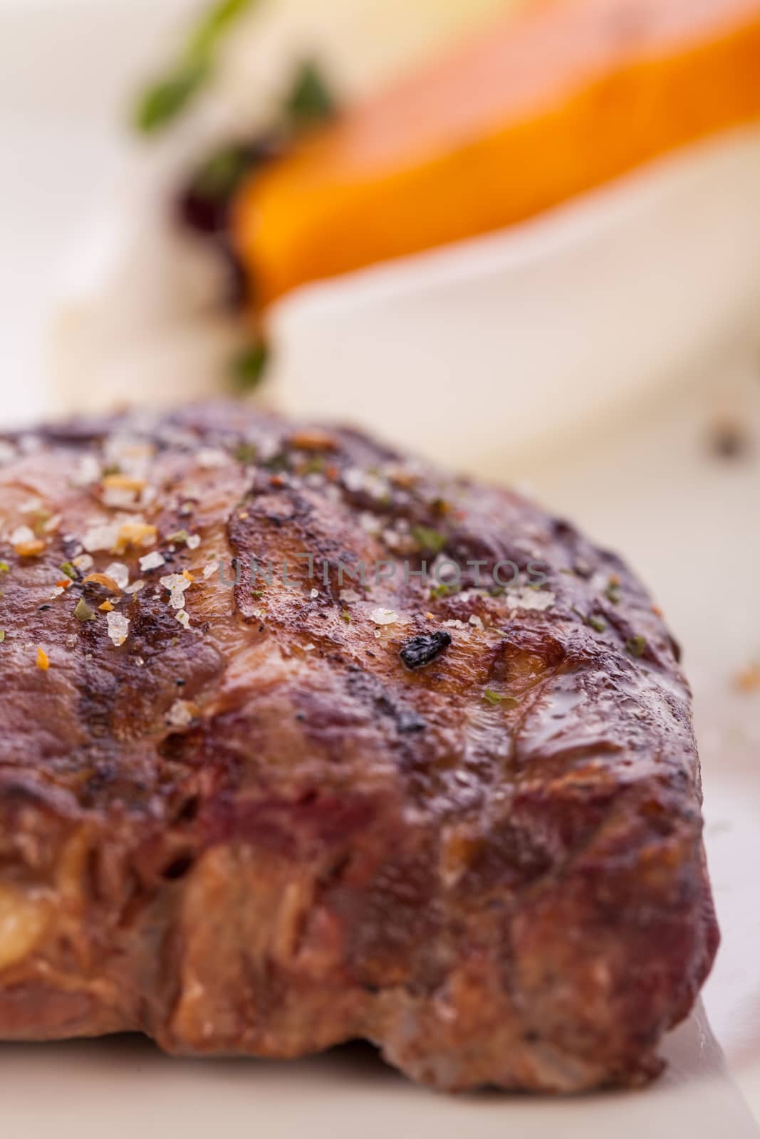 Delicious trimmed lean portion of thick grilled beef steak with seasoning served on a white plate, close up with shallow dof