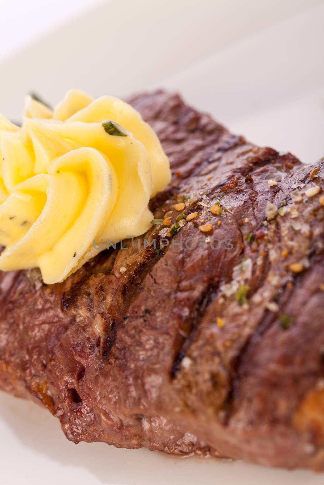 Tasty grilled beef steak topped with a twirled knob of butter and a sprig of fresh rosemary and served on a white plate, close up view