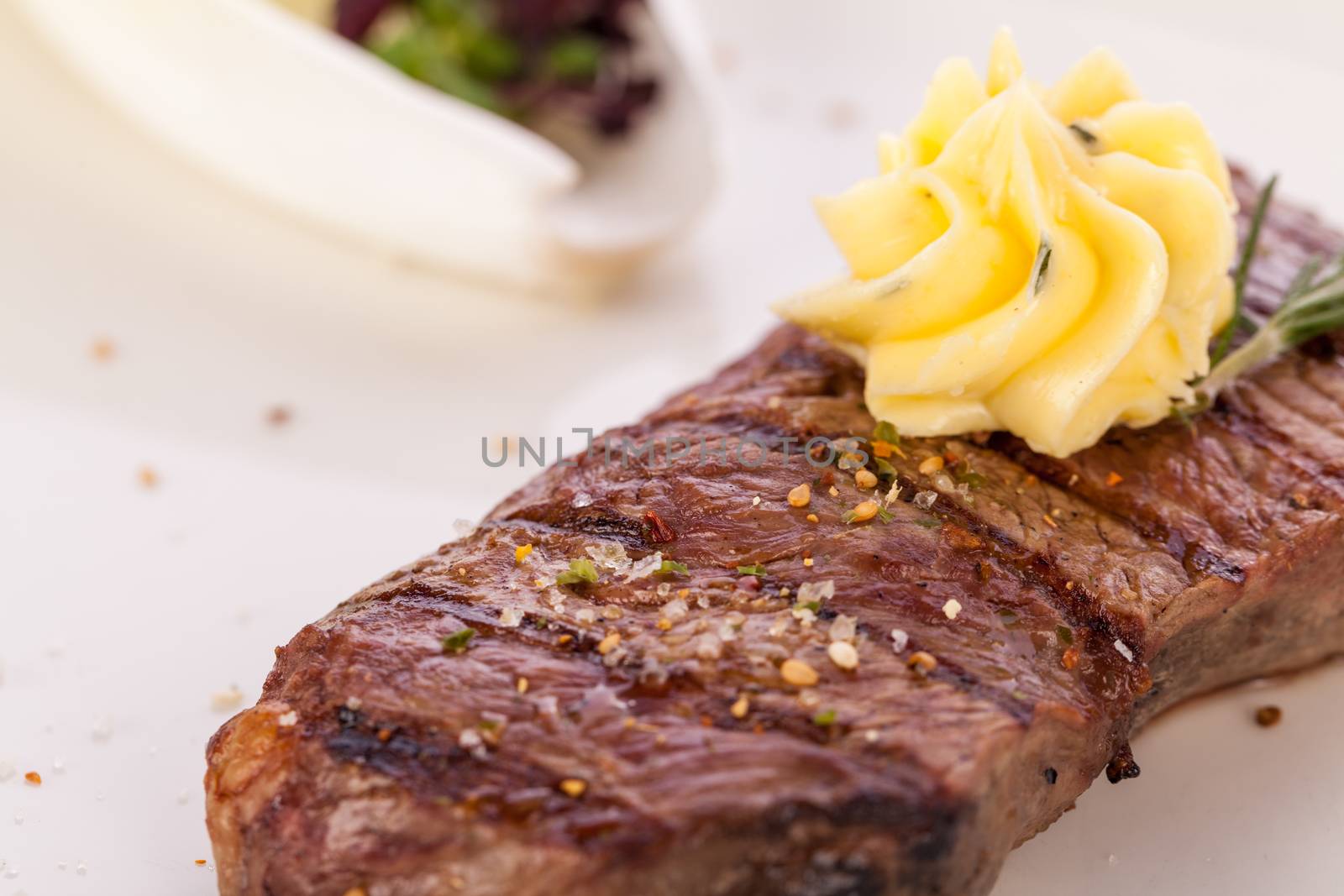 Tasty grilled beef steak topped with a twirled knob of butter and a sprig of fresh rosemary and served on a white plate, close up view