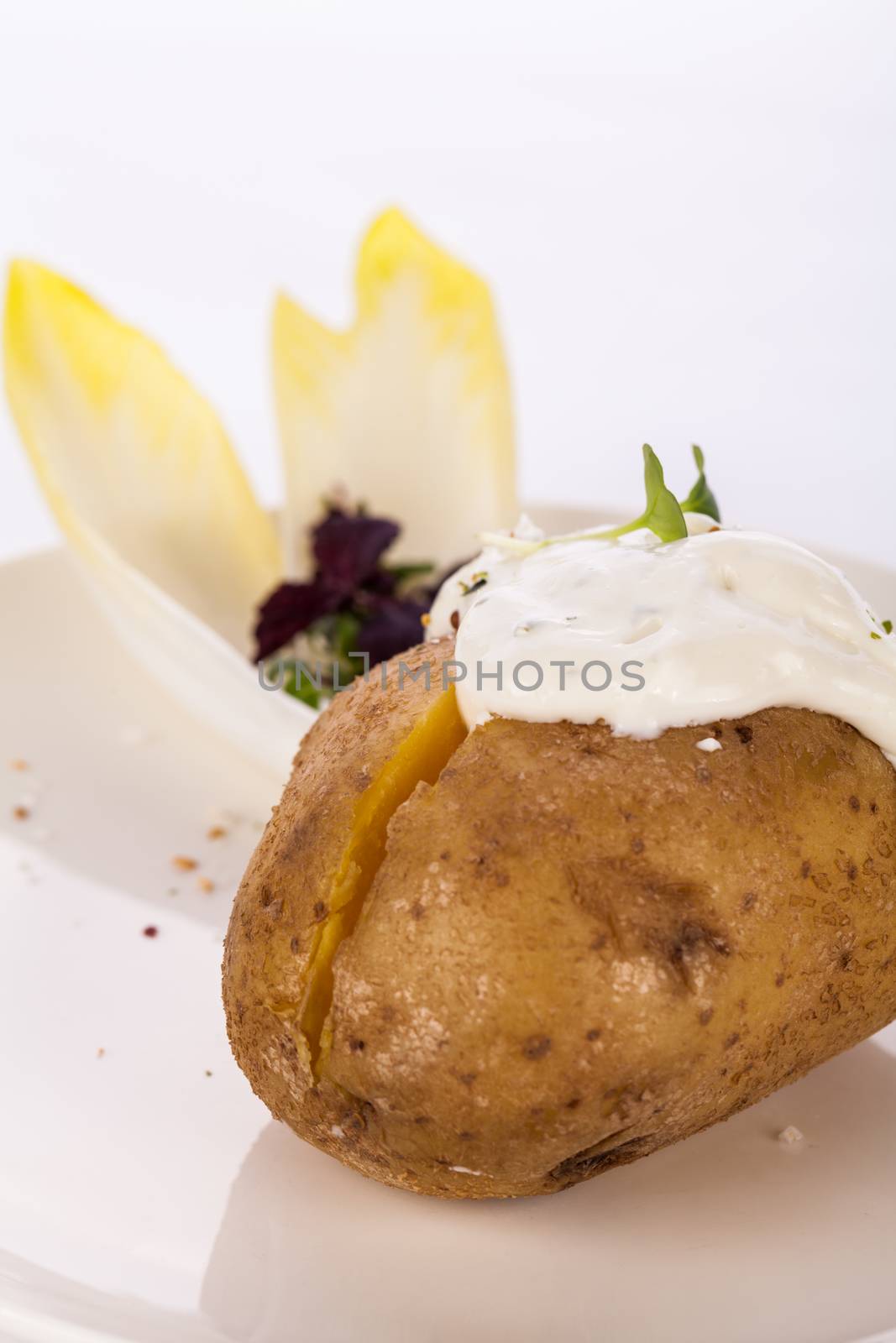 Overhead view of a healthy oven baked jacket potato with sour cream sauce garnished with endive leaves and fresh herbs