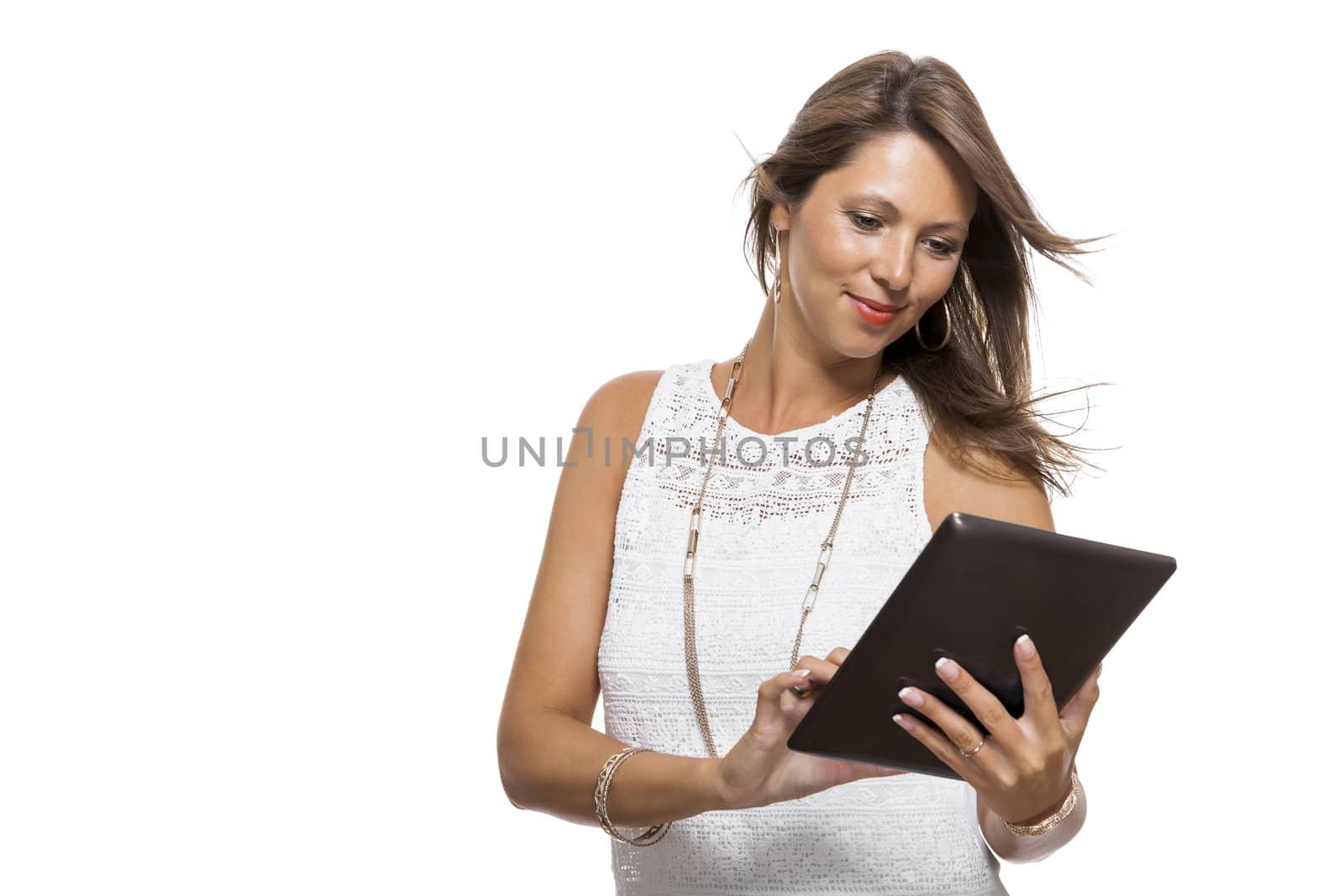 Attractive young business woman standing chatting on a mobile while simultaneously reading a tablet computer with a smile, isolated on white