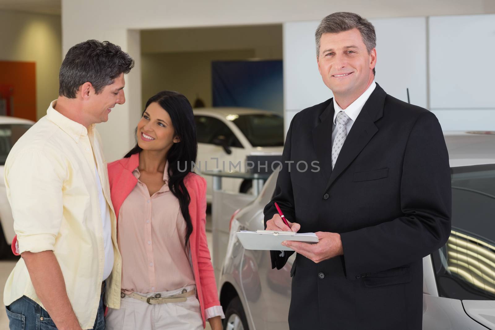 Businessman smiling at camera while writing on clipboard at new car showroom