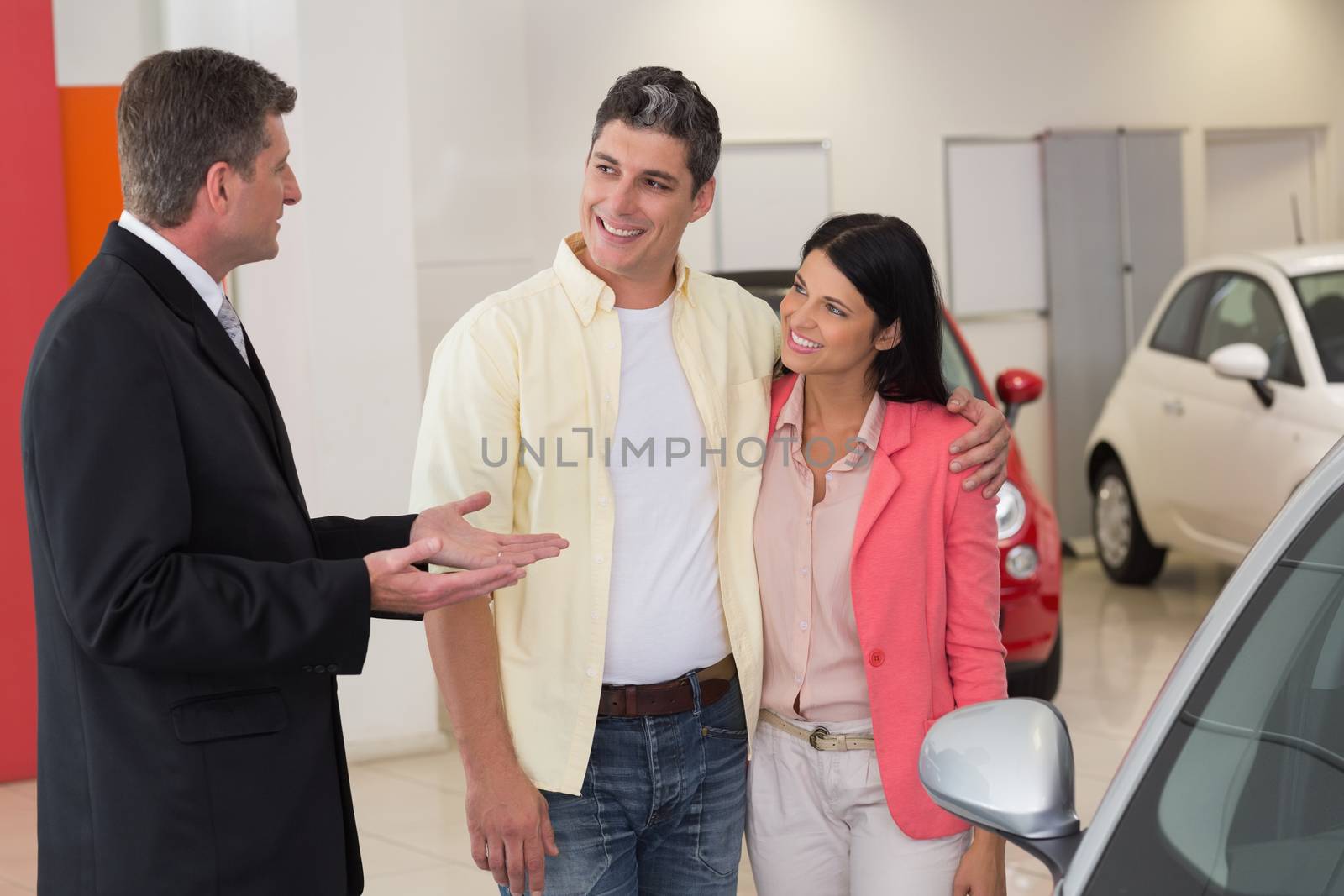 Smiling businessman speaking with his customers at new car showroom