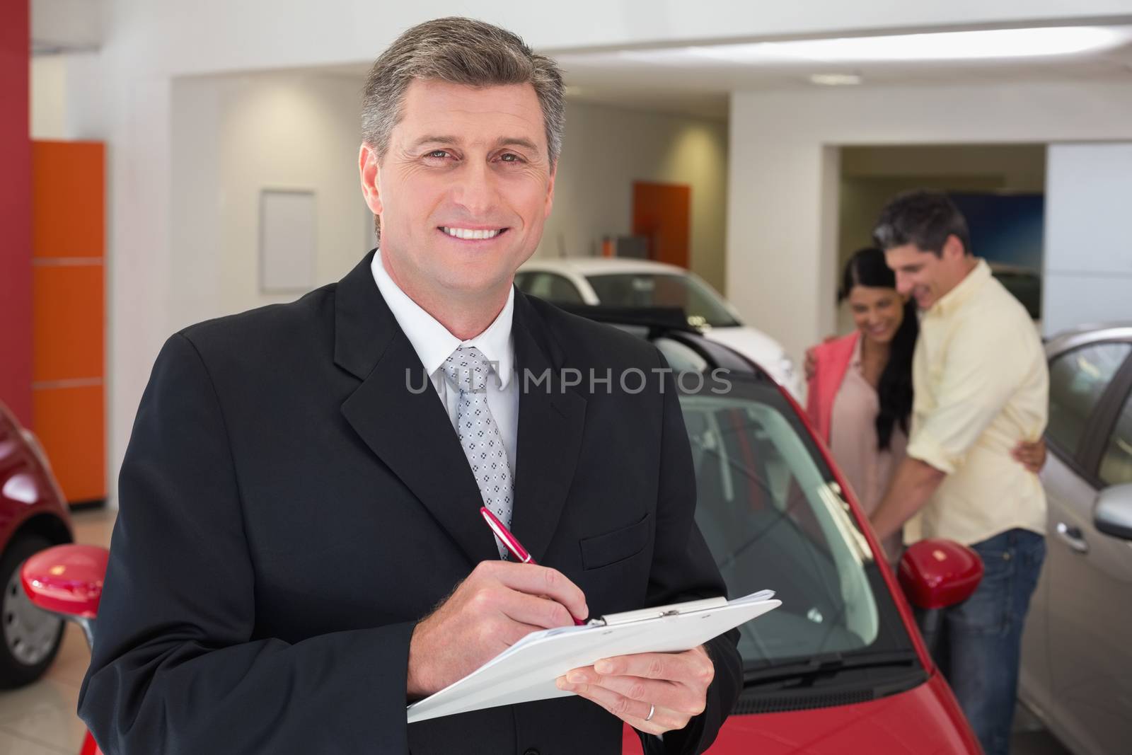 Smiling businessman writing on clipboard at new car showroom