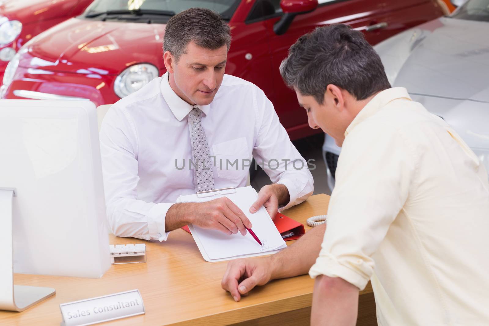 Salesman showing client where to sign the deal at new car showroom