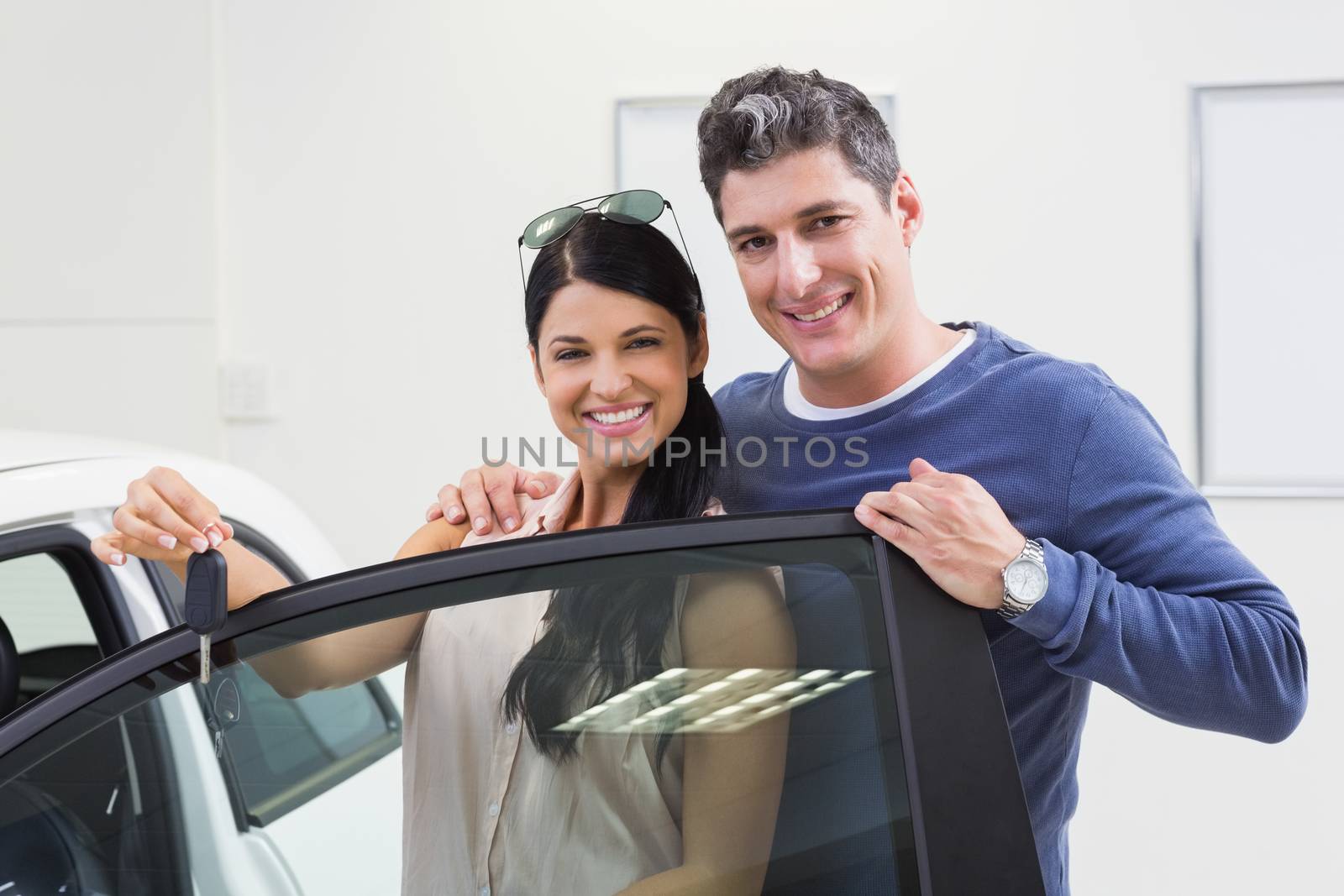 Smiling couple holding their new car key at new car showroom