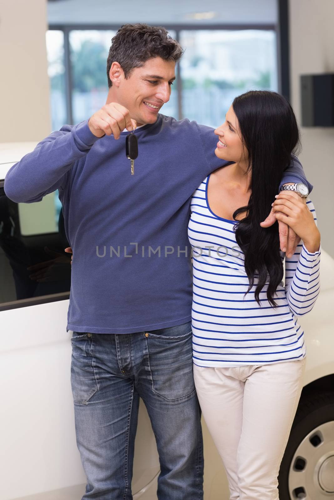 Smiling couple holding their new car key at new car showroom