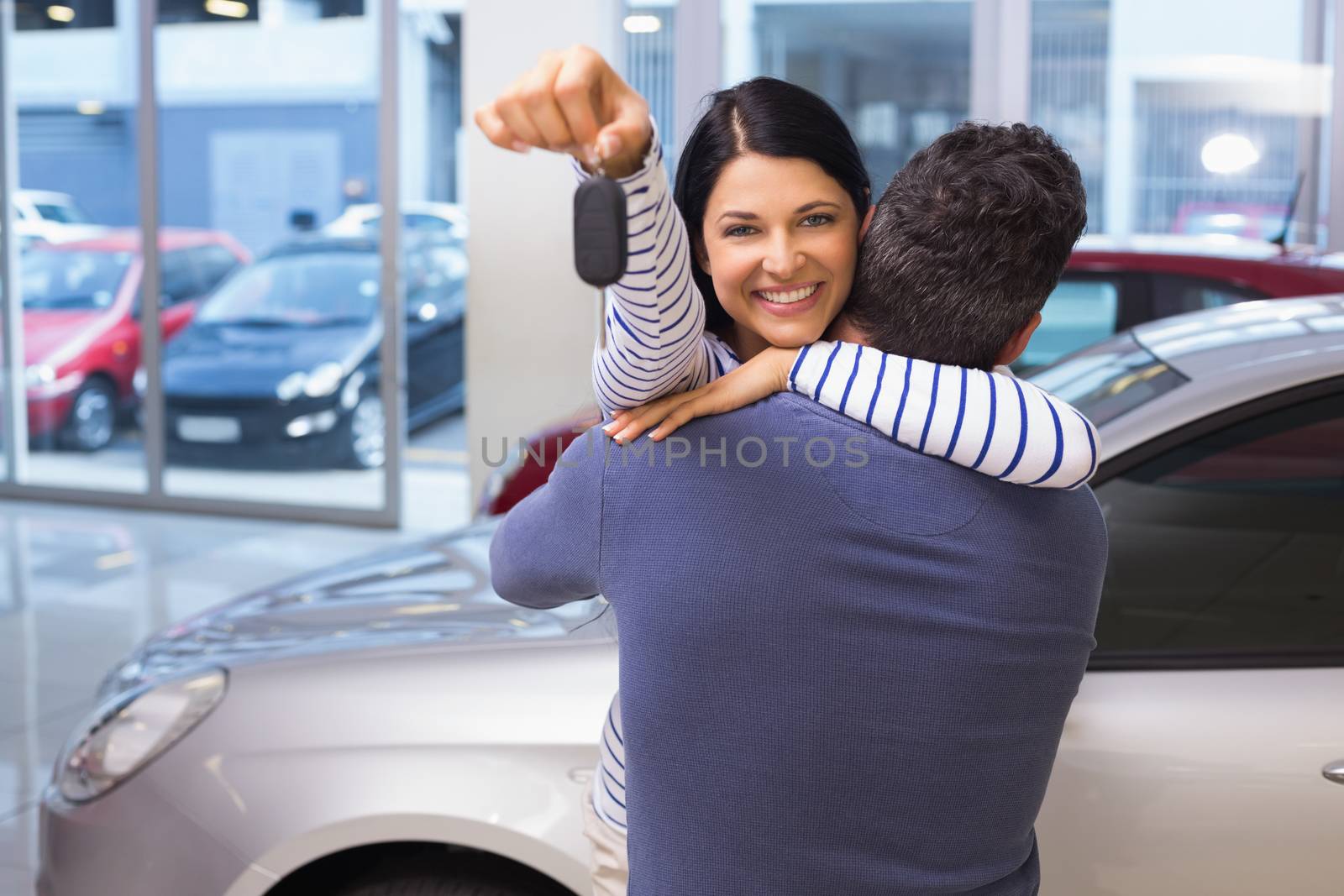 Smiling couple hugging and holding their new key at new car showroom