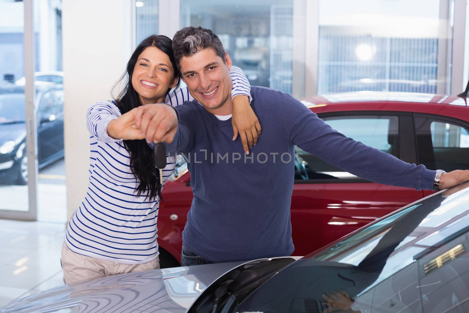 Smiling couple holding their new key at new car showroom