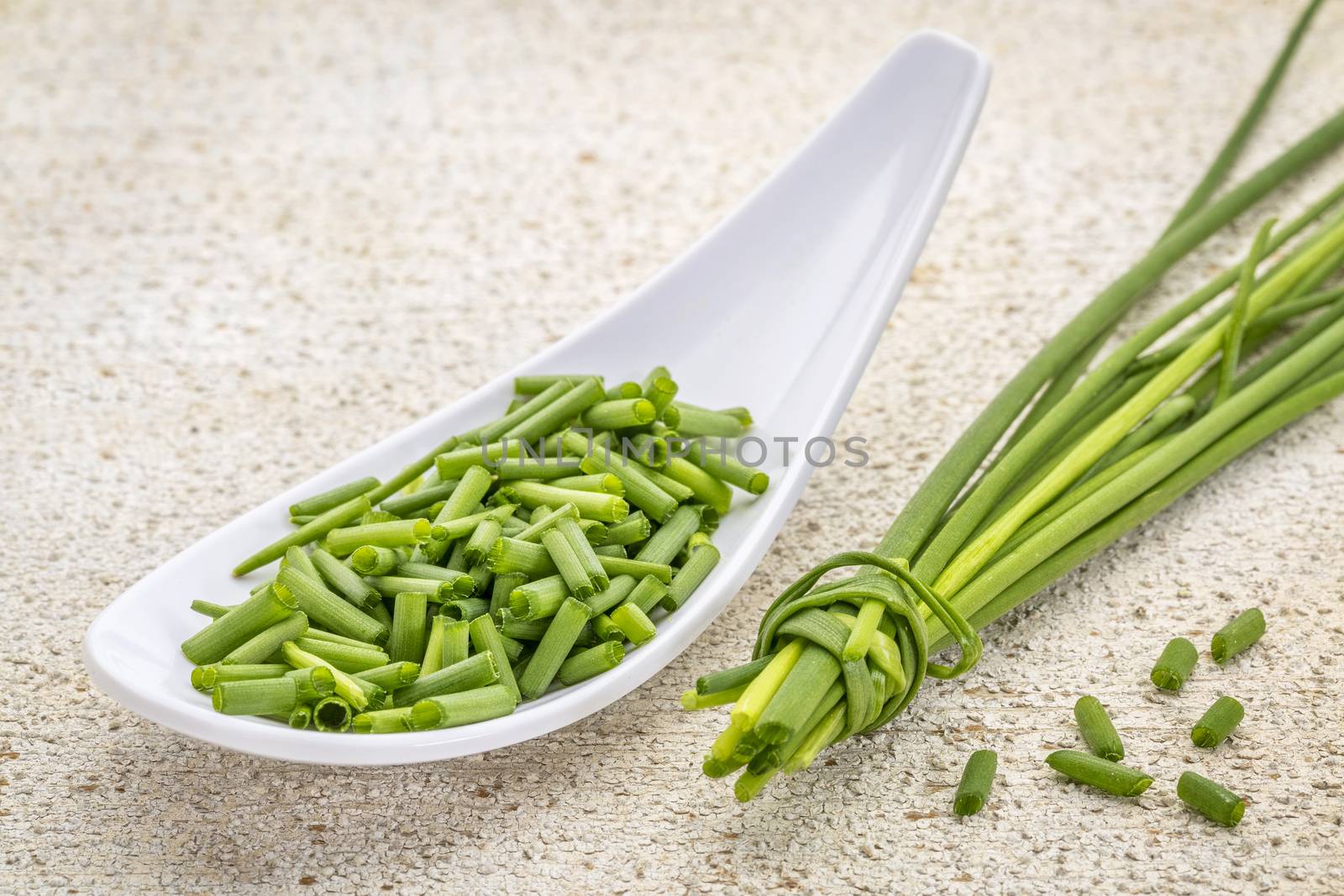 a spoon of chopped fresh chives with a bunch against withe painted barn wood