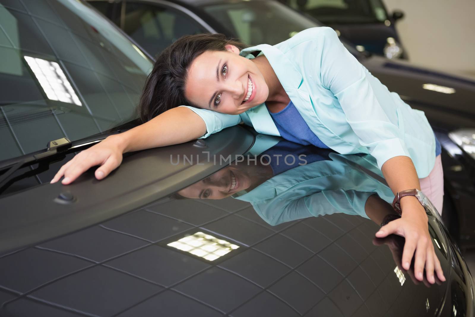 Smiling woman hugging a black car at new car showroom