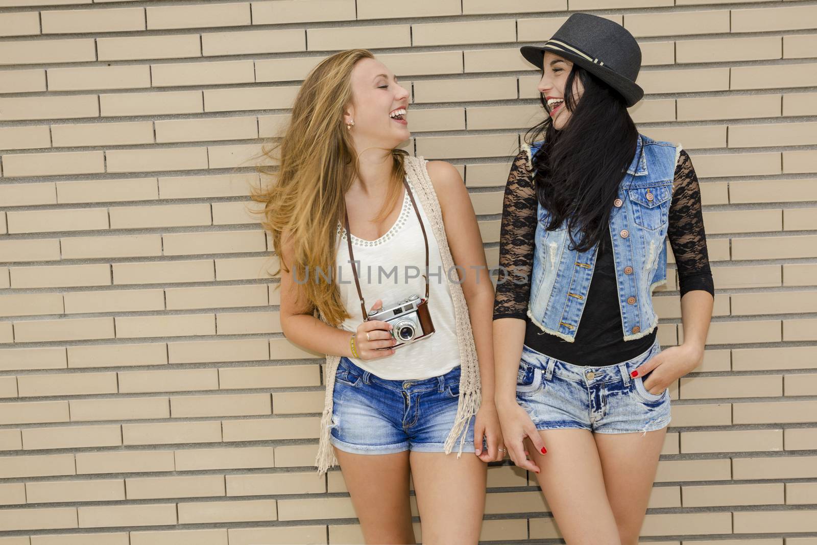 Two beautiful and young girlfriends having fun, in front of a brick wall