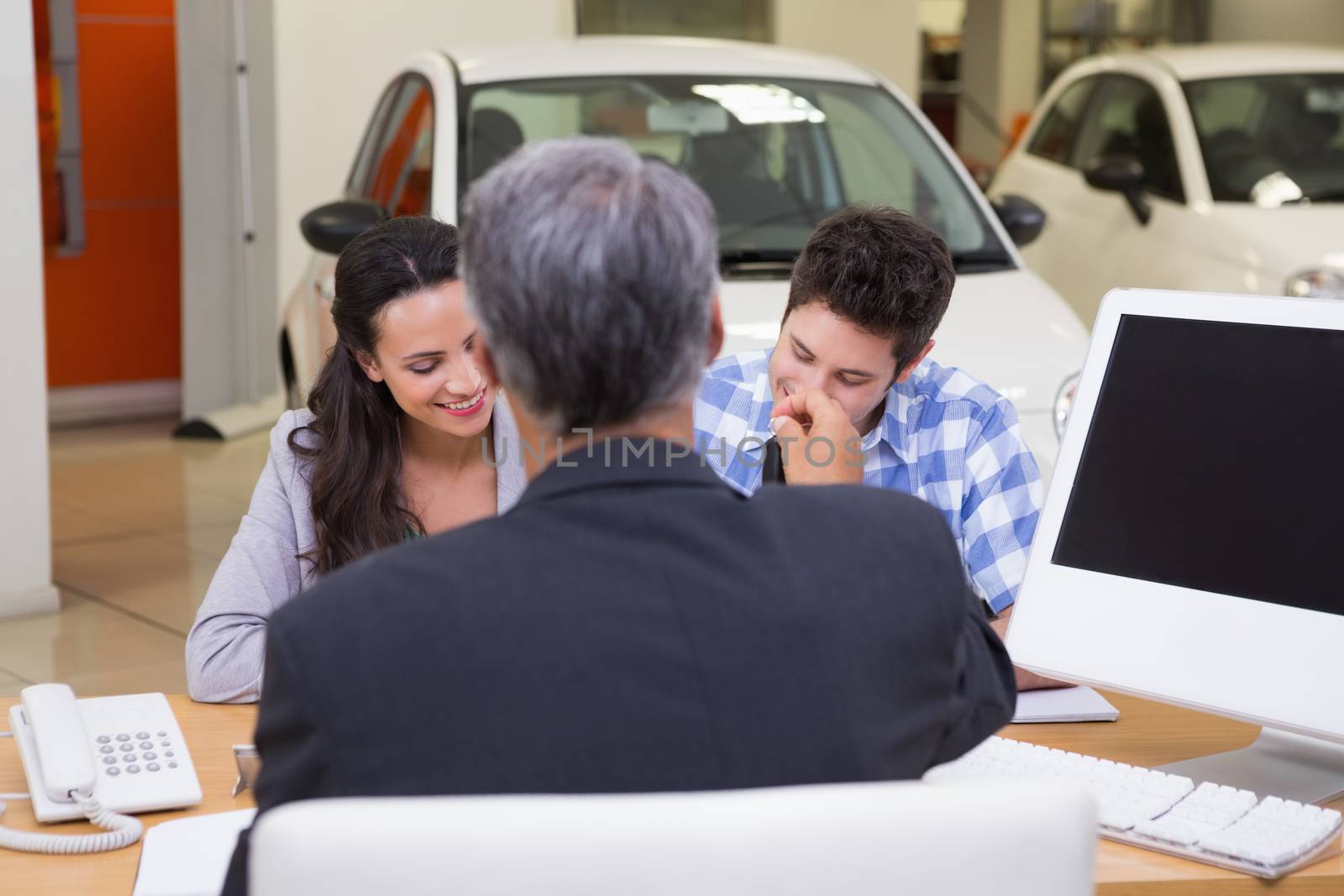 Smiling couple signing a contract at new car showroom